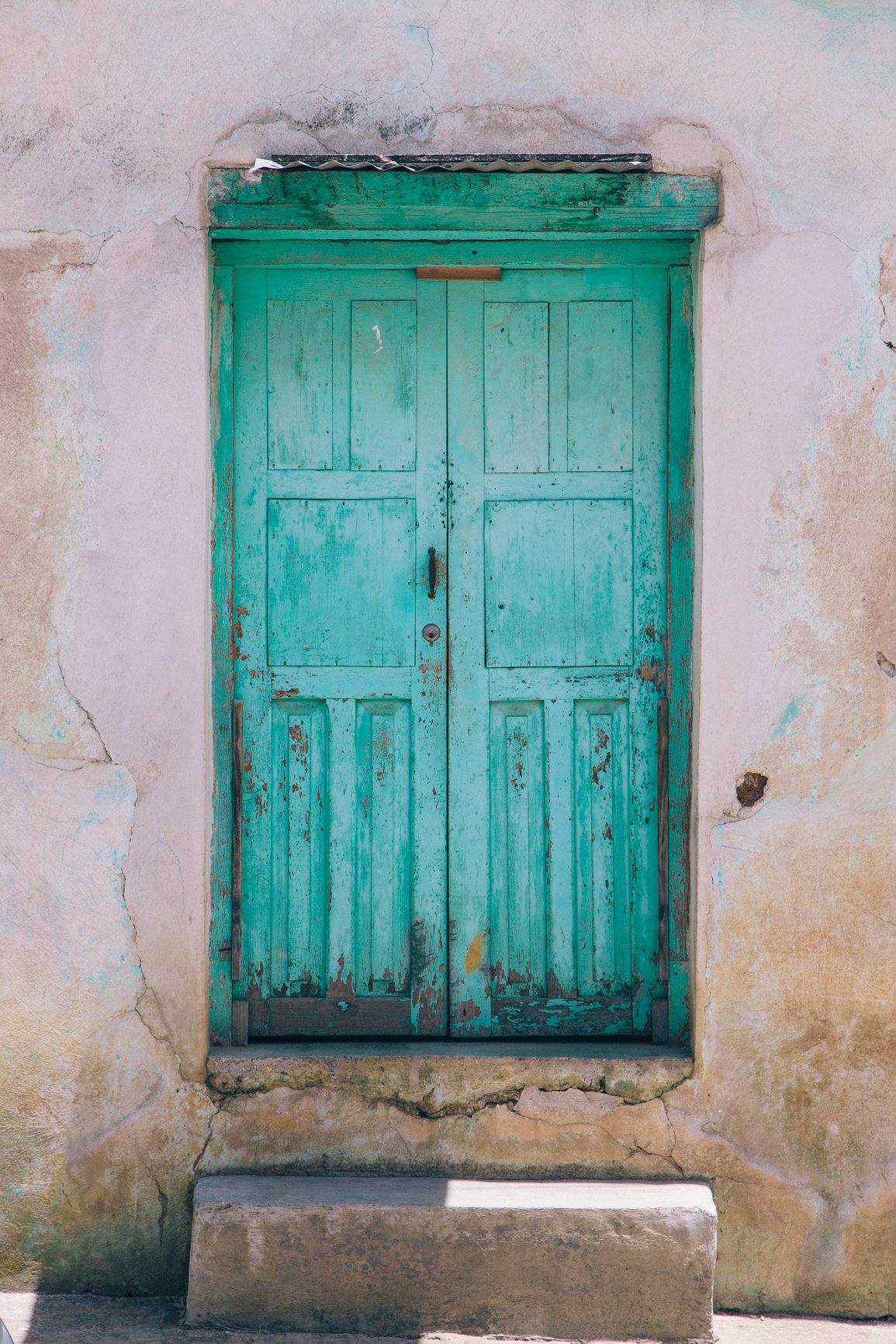 Weathered turquoise wooden doors set within an aged stucco wall, symbolizing healing, reflection, and new possibilities.