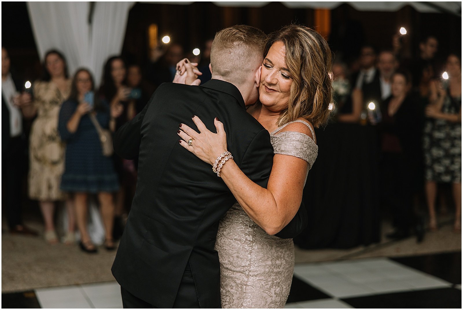 A mother and son dance close while guests watch from the side of the dance floor.