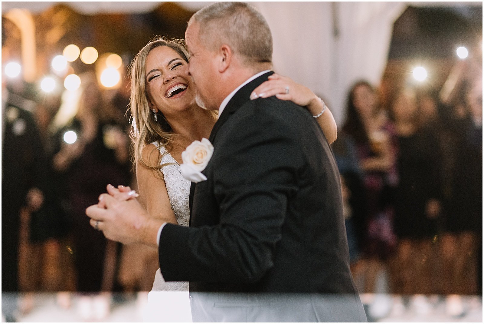 A bride laughs while she dances with her father.