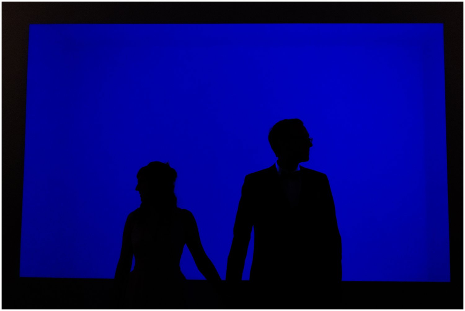 A bride and groom pose in front of a blue screen at a Mattress Factory wedding.