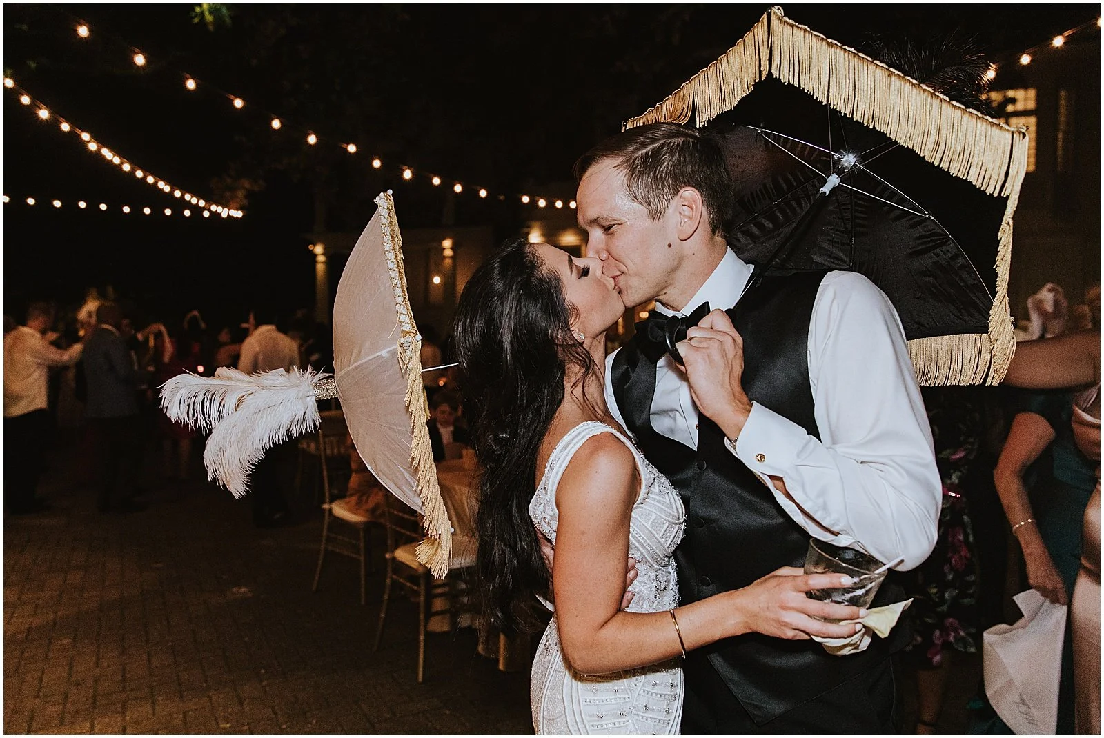 A bride and groom carrying New Orleans wedding umbrellas lean towards each other to kiss.