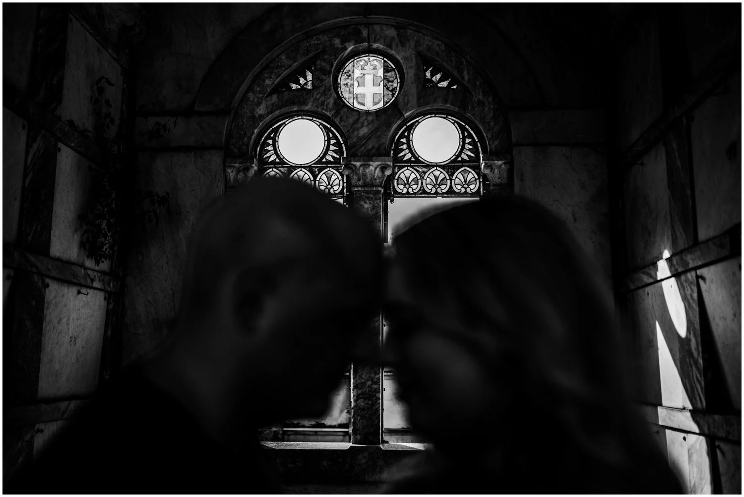 An engaged couple is silhouetted against a stained glass window in a New Orleans engagement photo.