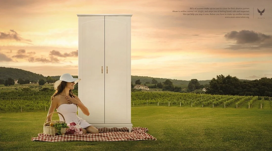 A woman sitting on a red and white checkered picnic blanket in a field, wearing a white dress and sun hat, with a basket of flowers beside her, and a white wardrobe behind her, with a scenic rural landscape and sunset in the background.