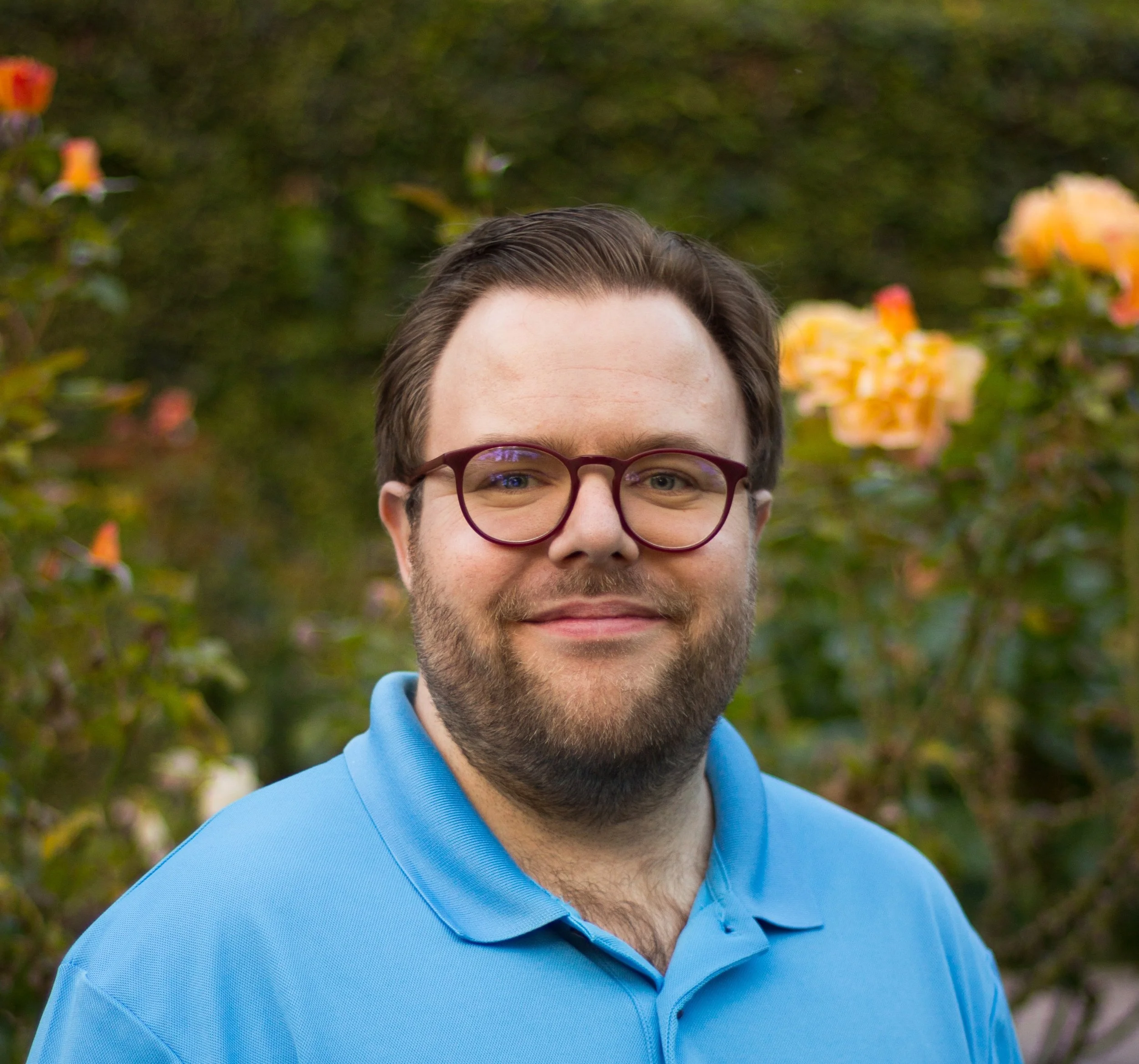 a bearded white man with light brown hair and glasses wearing a blue collared shirt