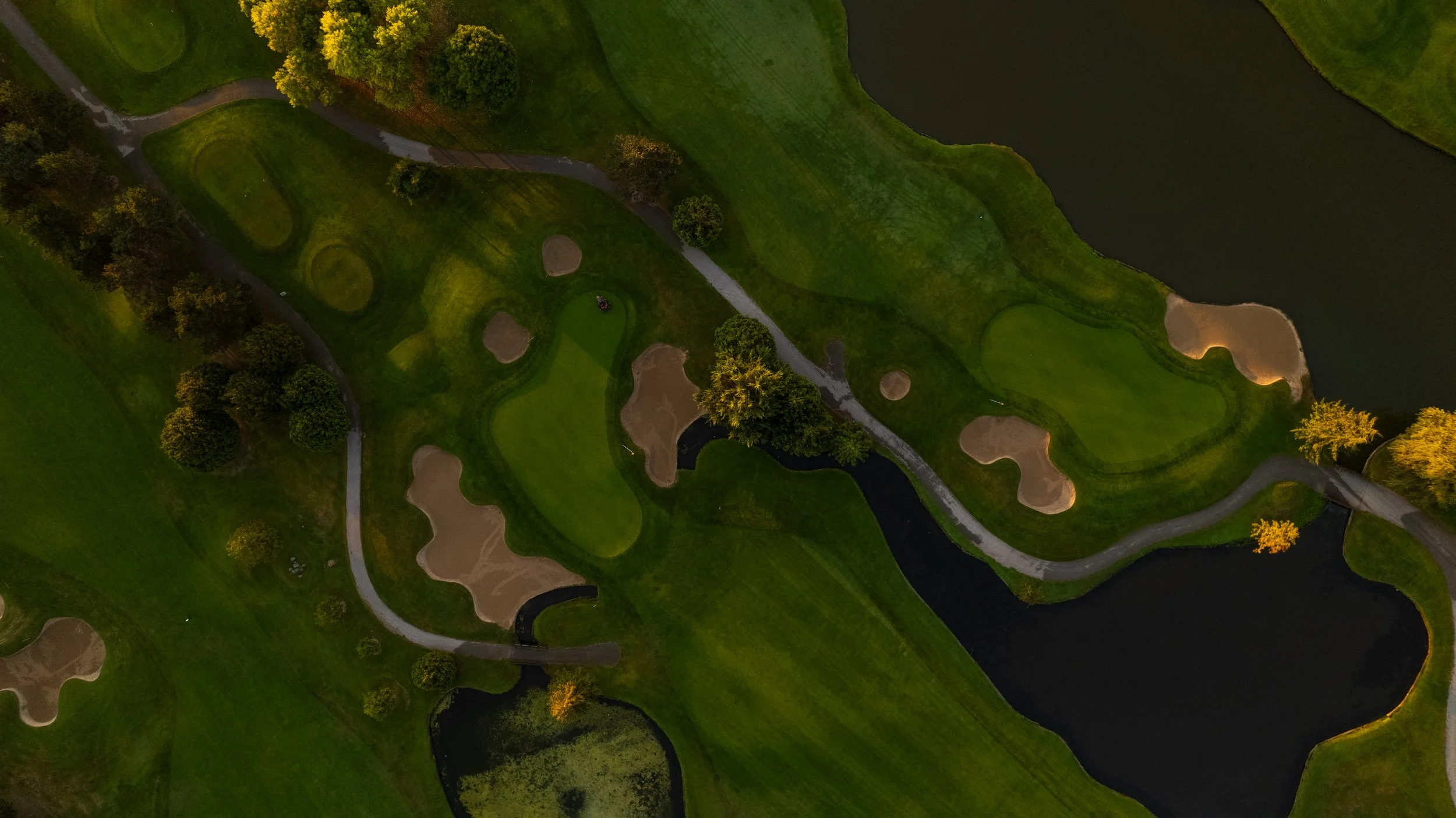 Aerial view of a golf course featuring multiple fairways, greens, sand bunkers, water hazards, and trees.