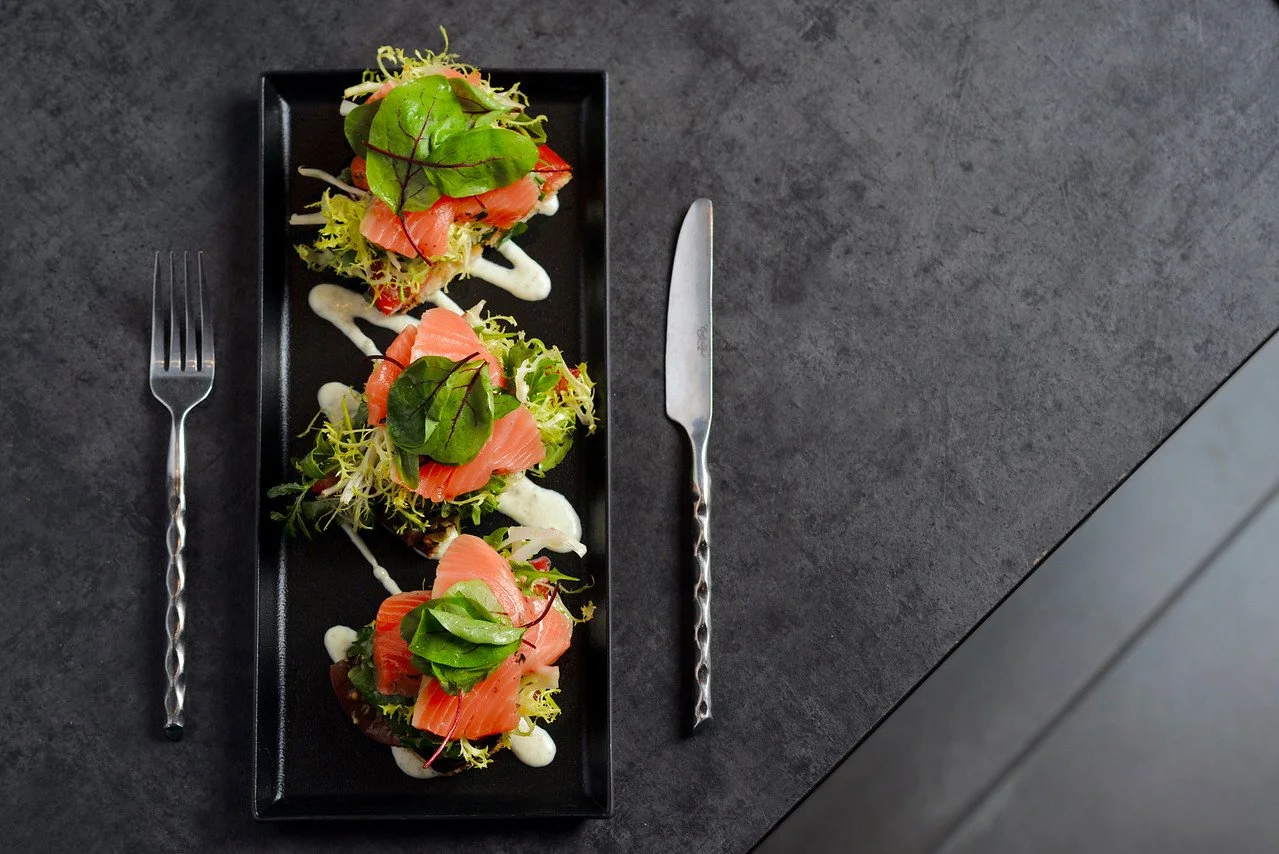 Overhead image of smoked salmon toast with greens and cream drizzle on black plate, photographed by Chad Chisholm Creative for restaurant marketing.