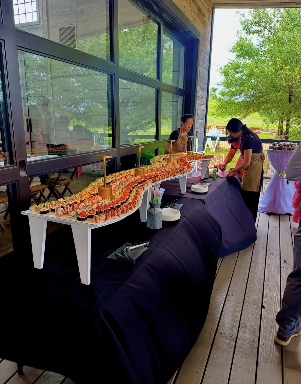 A sushi catering table set up on an outdoor deck surrounded by greenery