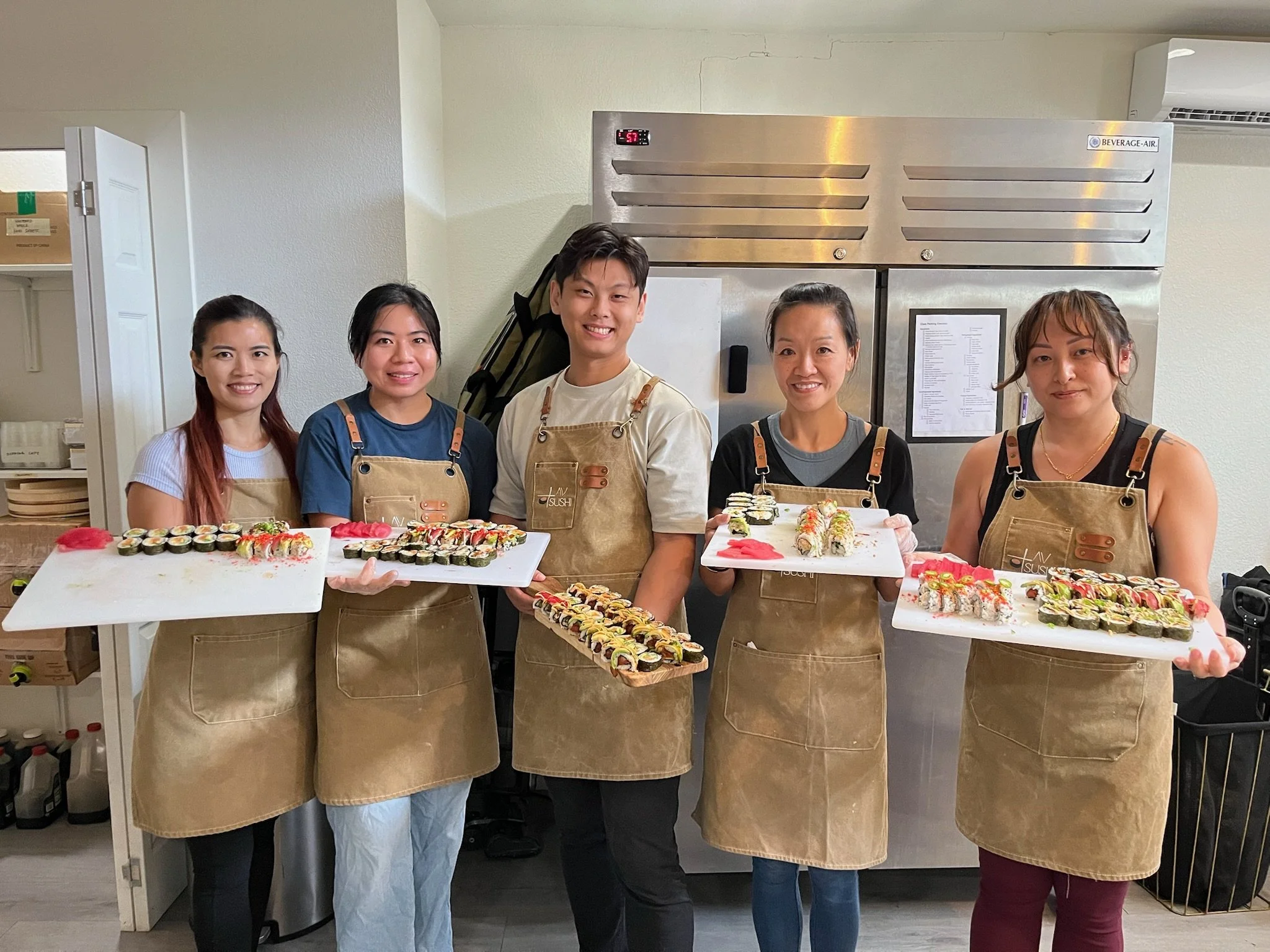 people smiling with sushi platters in hand in front of fridges
