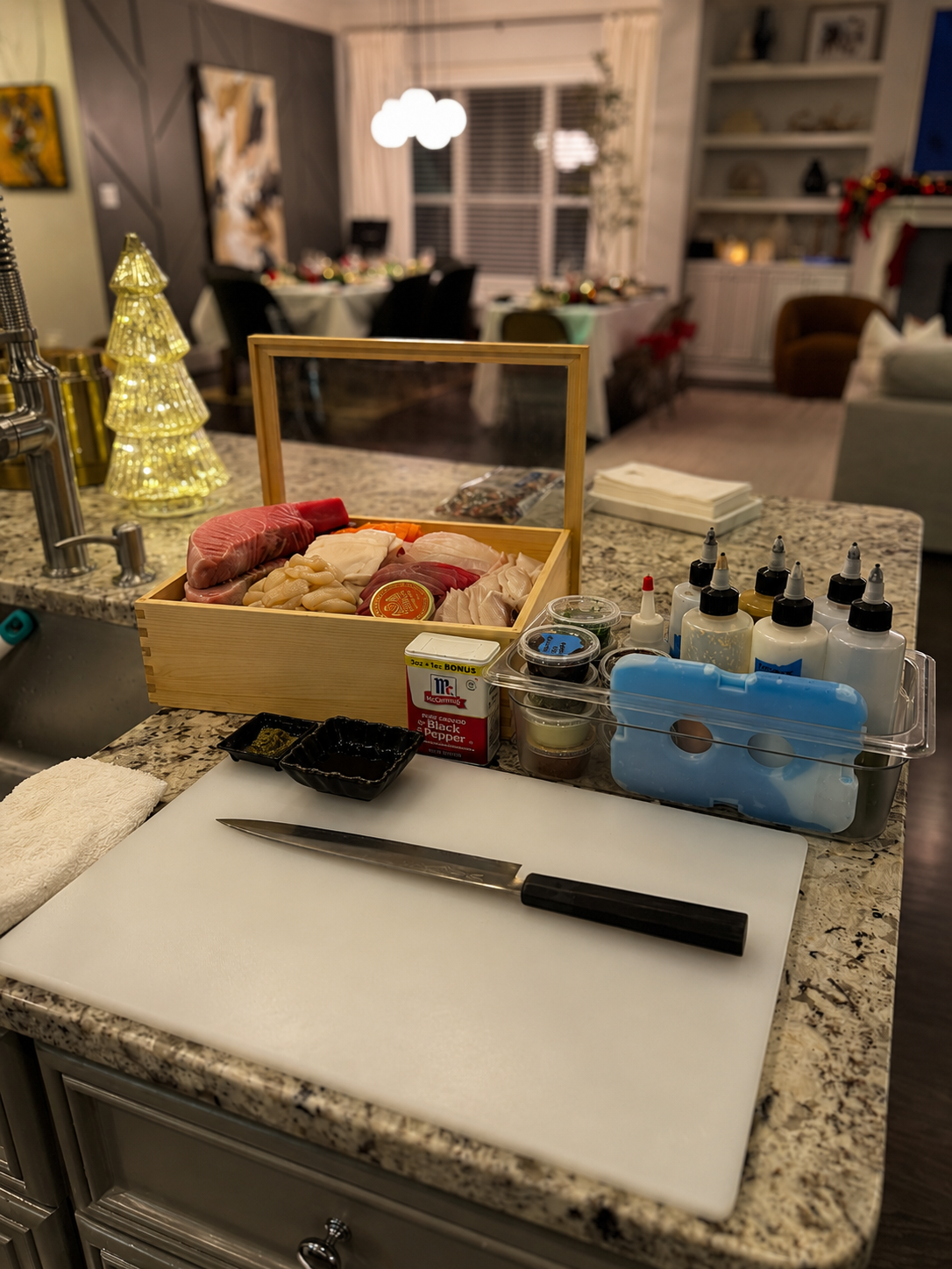 In-home omakase prep station with a chef's knife, cutting board, sauces, and a box of fresh sushi-grade fish
