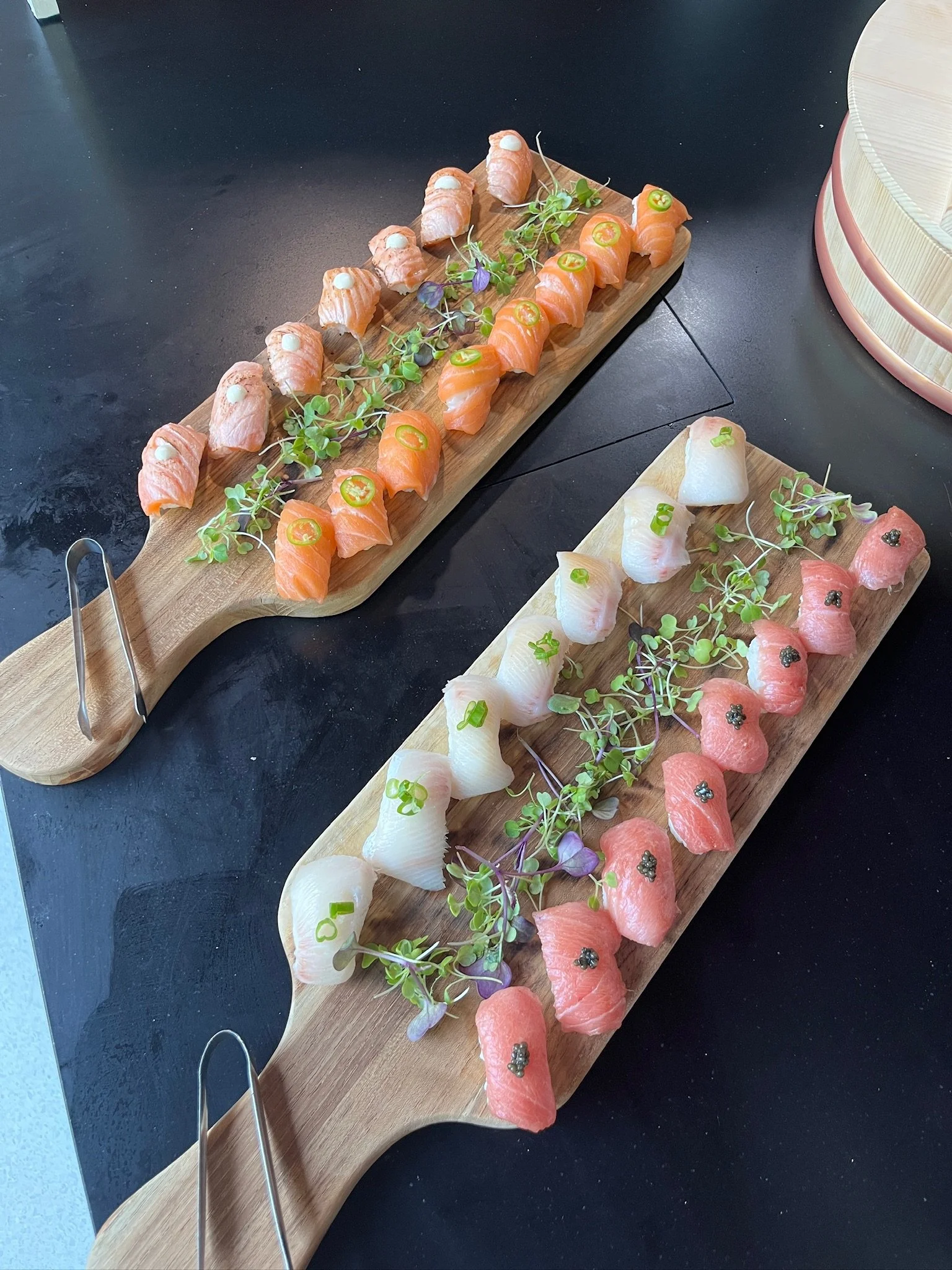 A row of nigiri sushi topped with salmon and garnish arranged on a serving board
