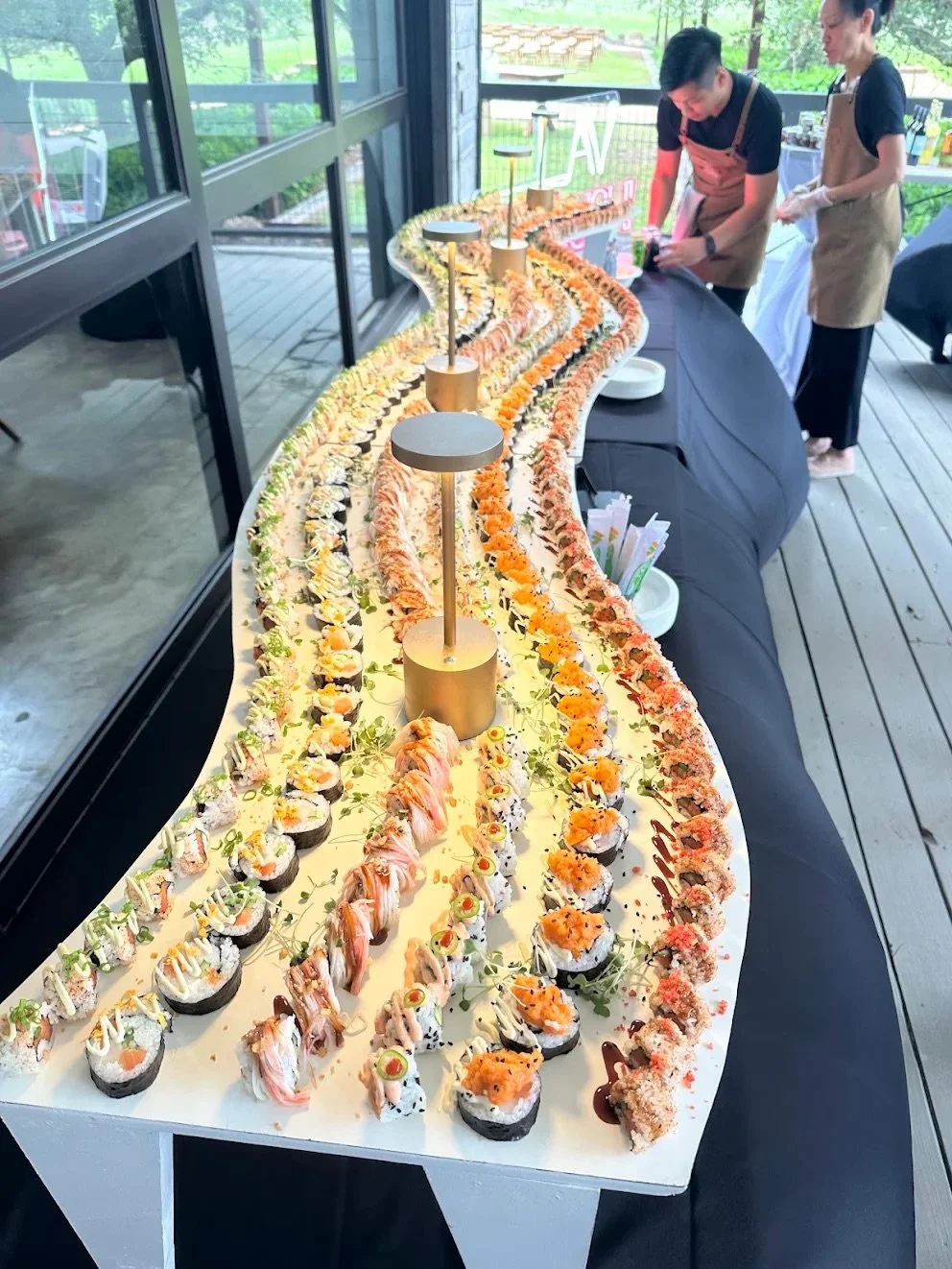 A long winding table display of assorted sushi rolls at an outdoor catering event