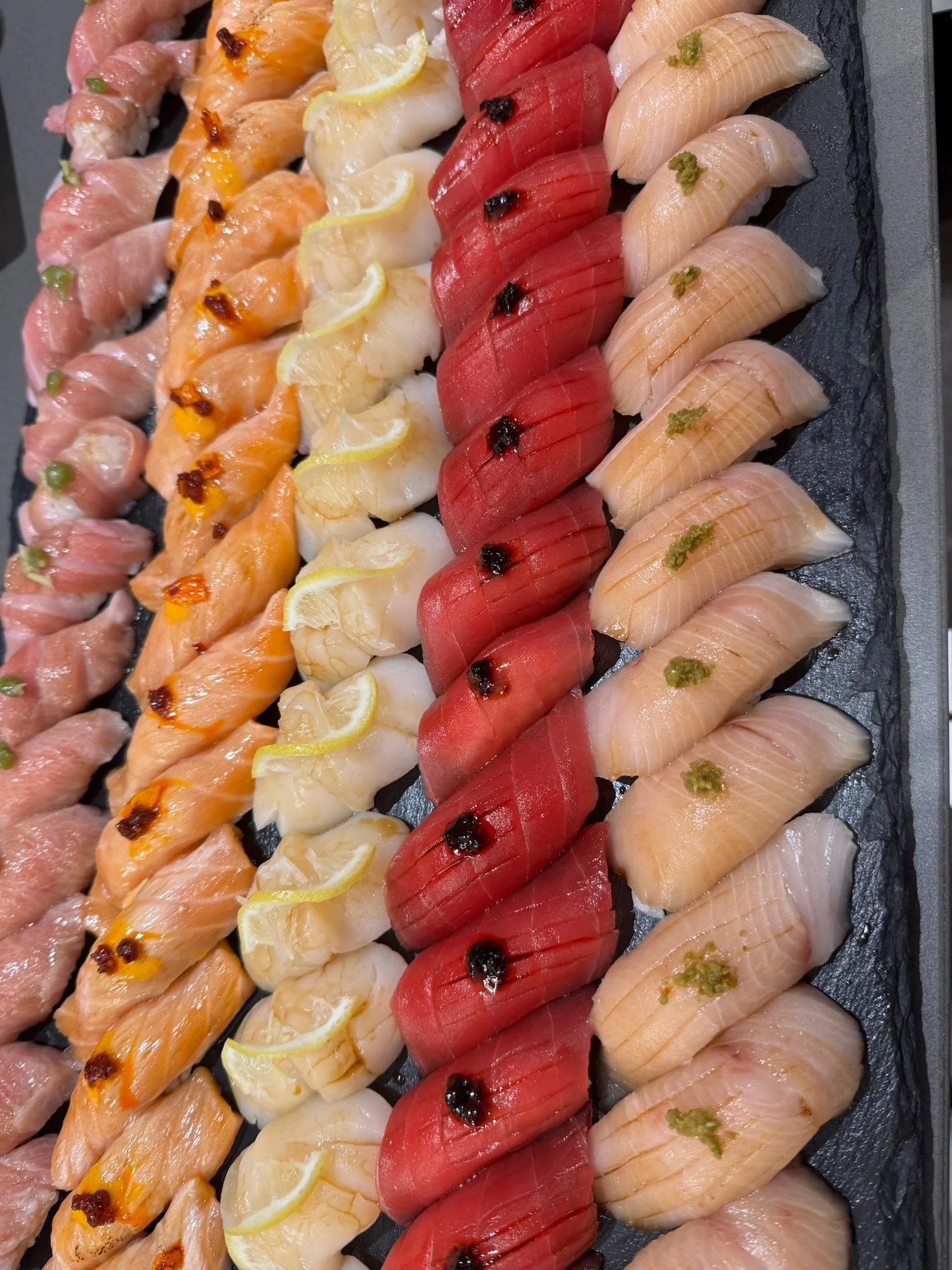 Rows of colorful nigiri sushi arranged in gradient stripes on a serving platter