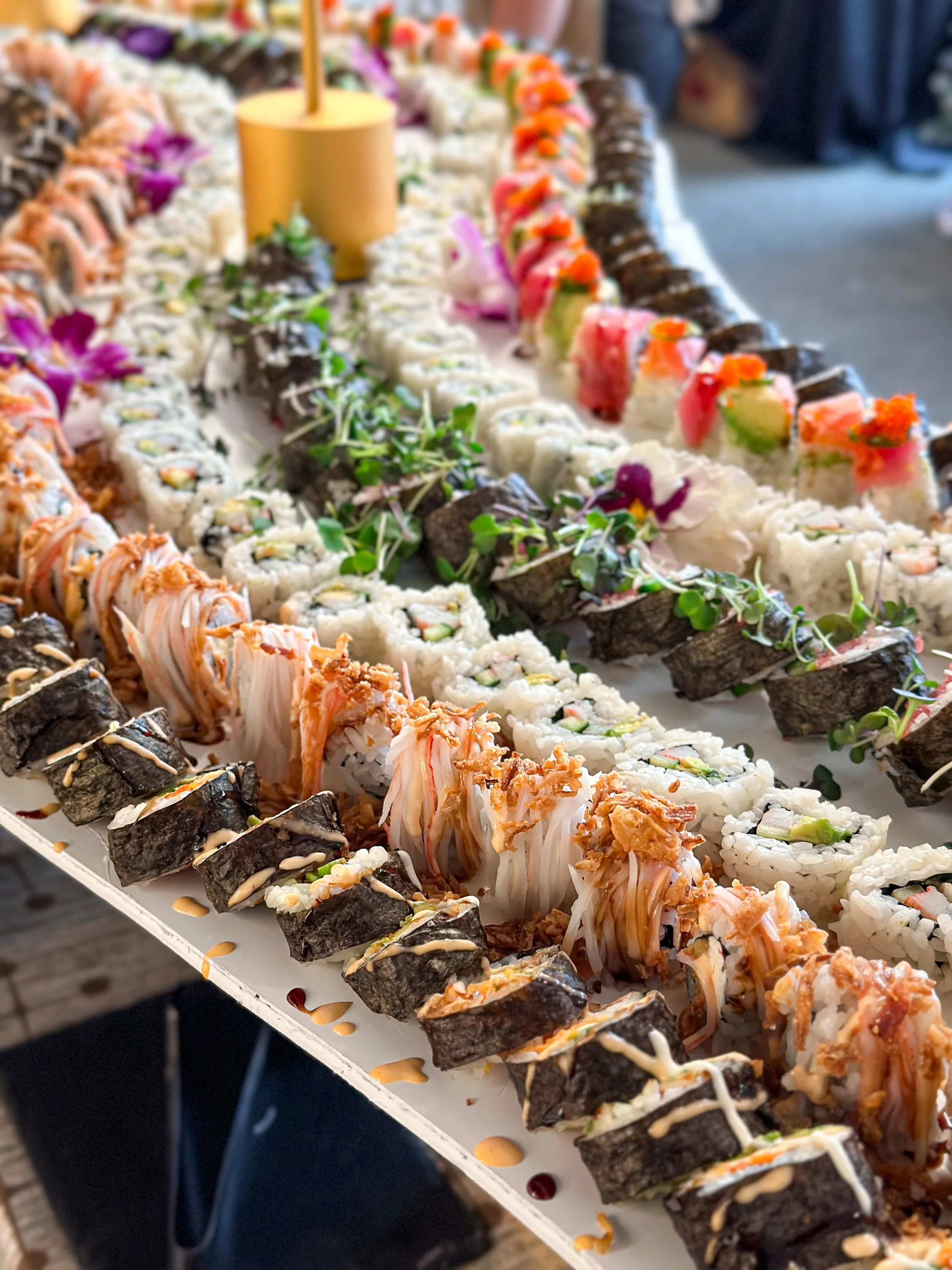 An elevated sushi roll display garnished with flowers for a catering event