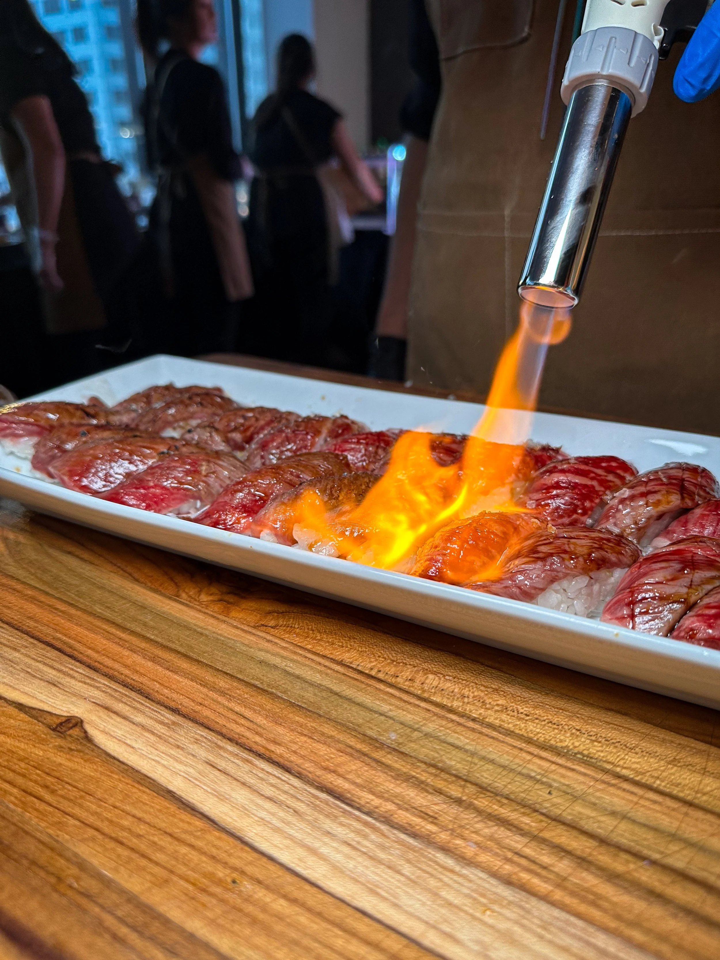 A chef using a kitchen torch to sear a sushi dish tableside at a catering event