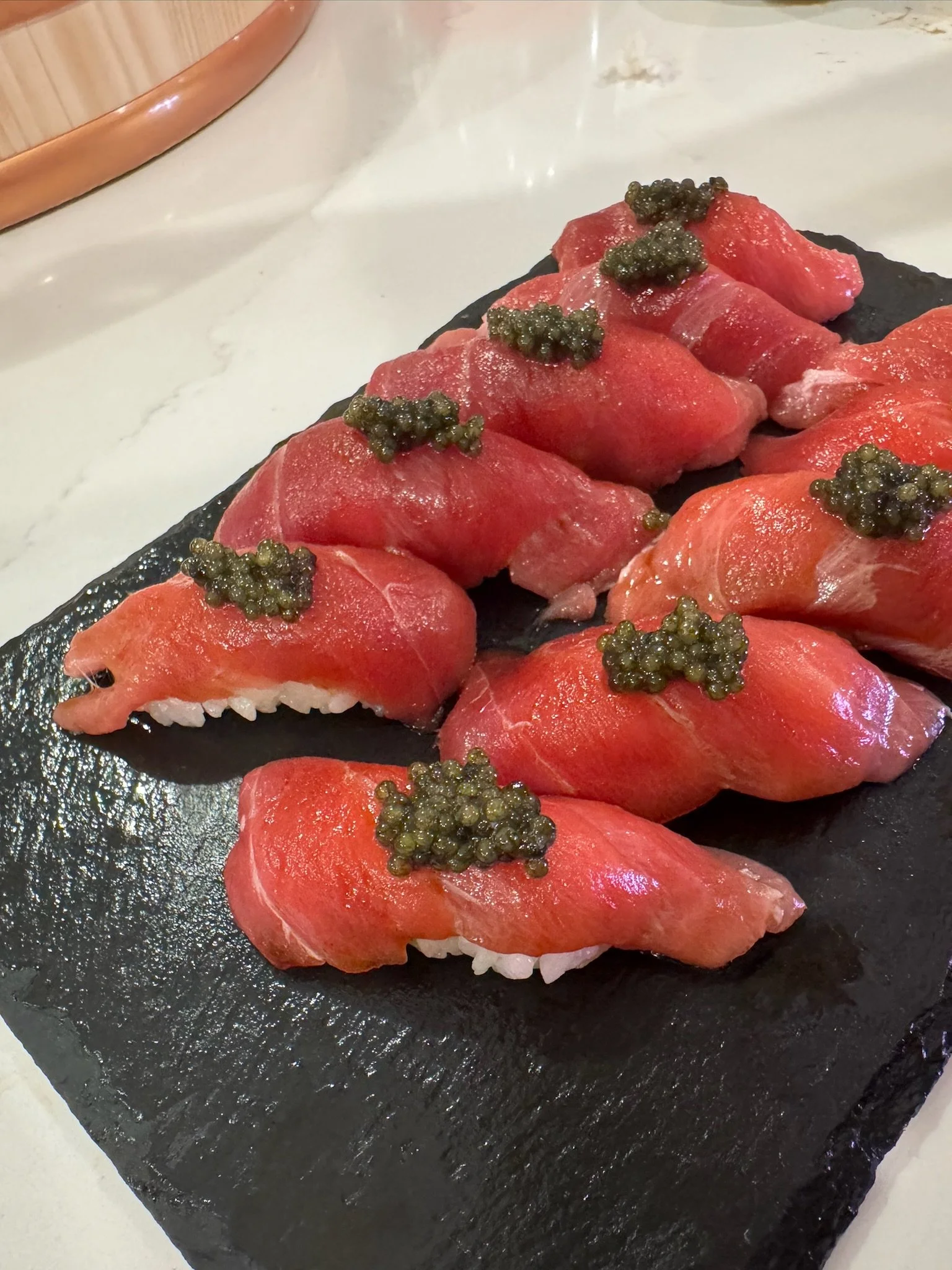 Tuna nigiri topped with caviar arranged on a black serving platter