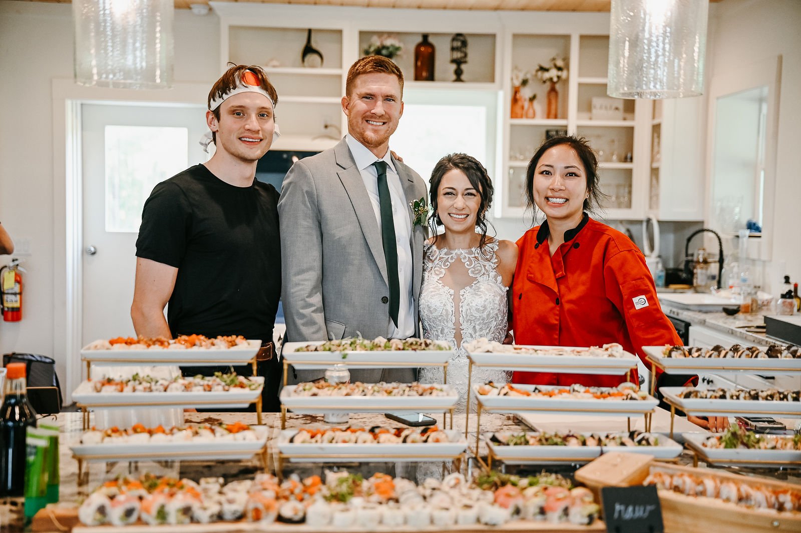 A chef and three guests smiling behind a table of catered sushi at a wedding event