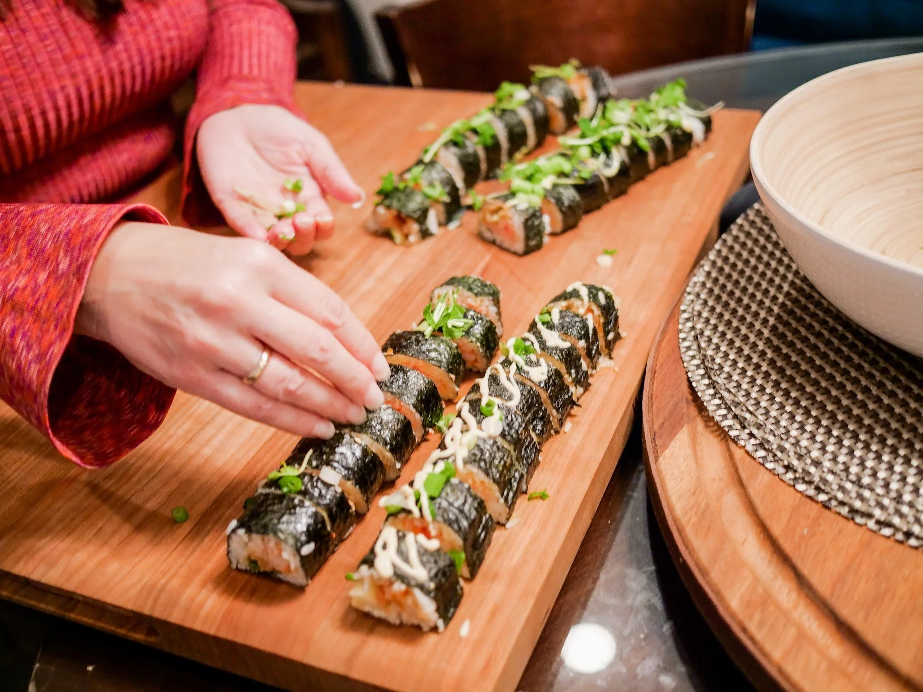 A chef plating freshly made sushi rolls on a wooden serving board