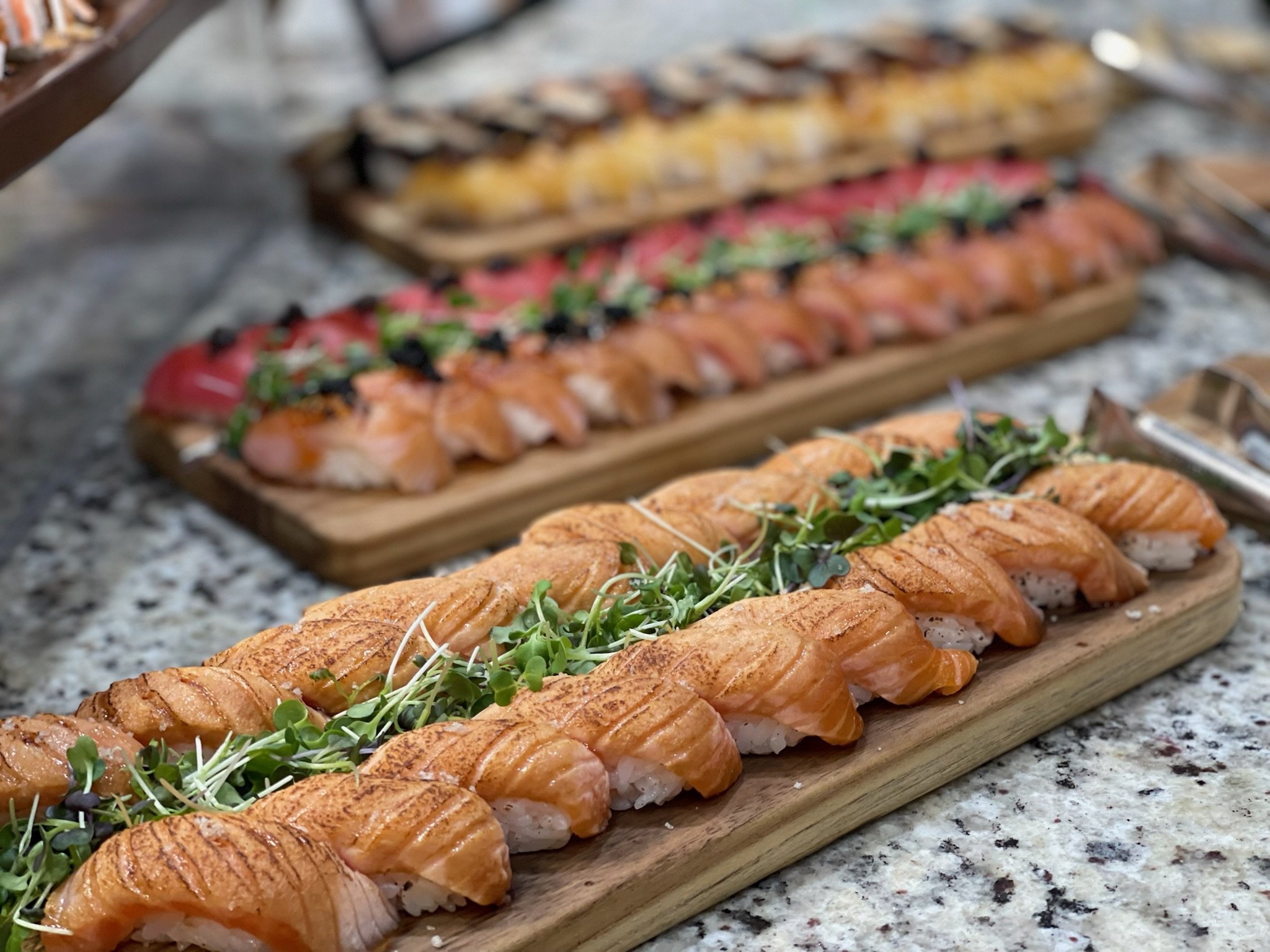 Close-up of three wooden serving boards filled with assorted sushi for sushi catering with LavSushi and sashimi on a speckled countertop.