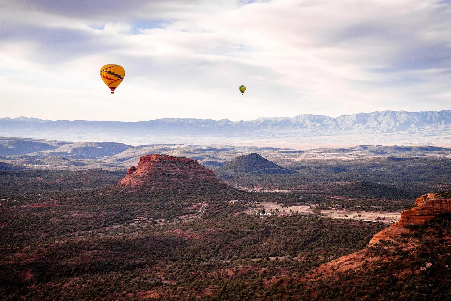Hot air balloons over Sedona's red rock landscape and distant mountains.