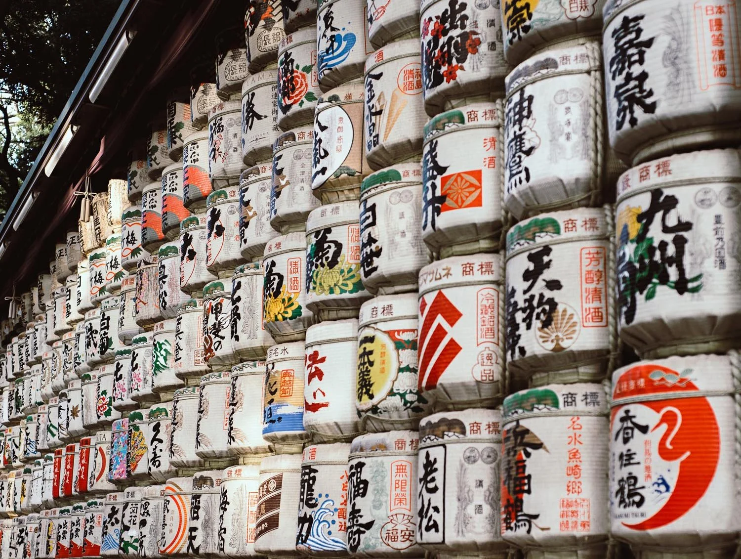 Traditional Japanese sake barrels stacked in rows, featuring colorful calligraphy and designs, often used as offerings at Shinto shrines.