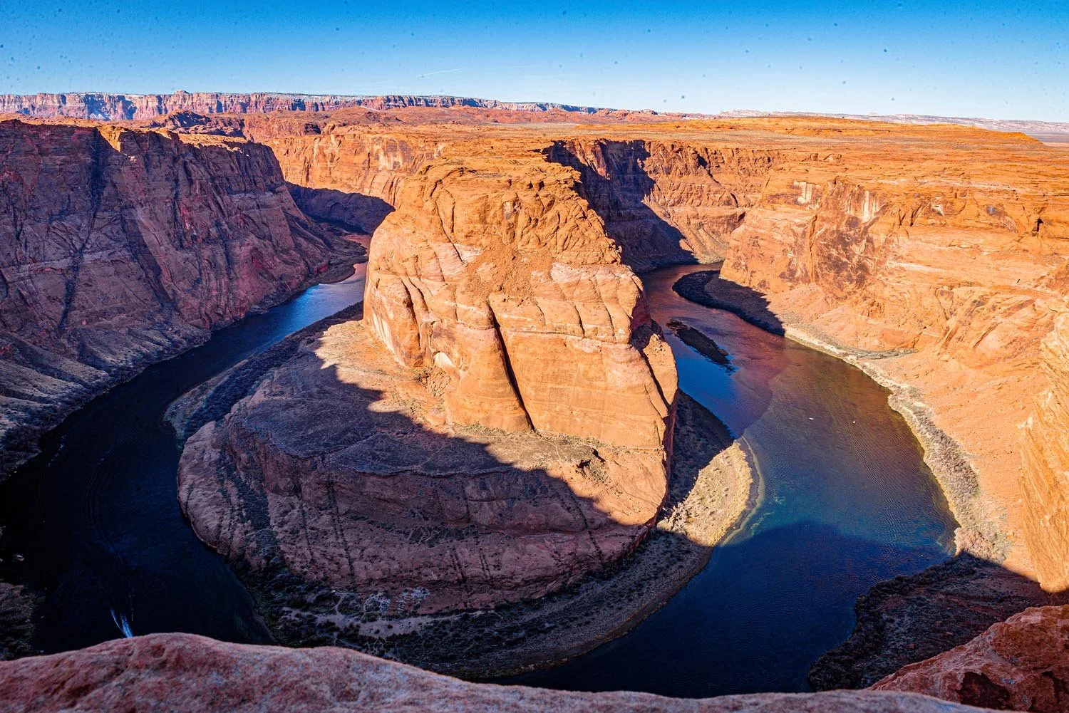 Horseshoe Bend in Arizona with Colorado River curving around red rock cliffs under a clear blue sky.