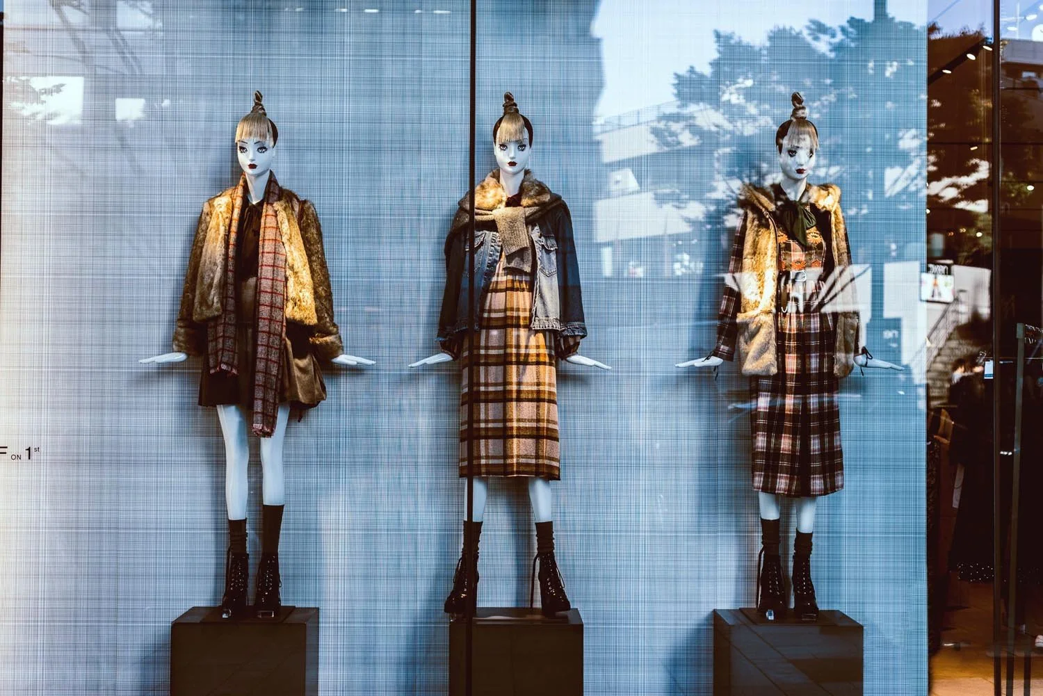 Storefront window display with three mannequins dressed in plaid outfits and layers.