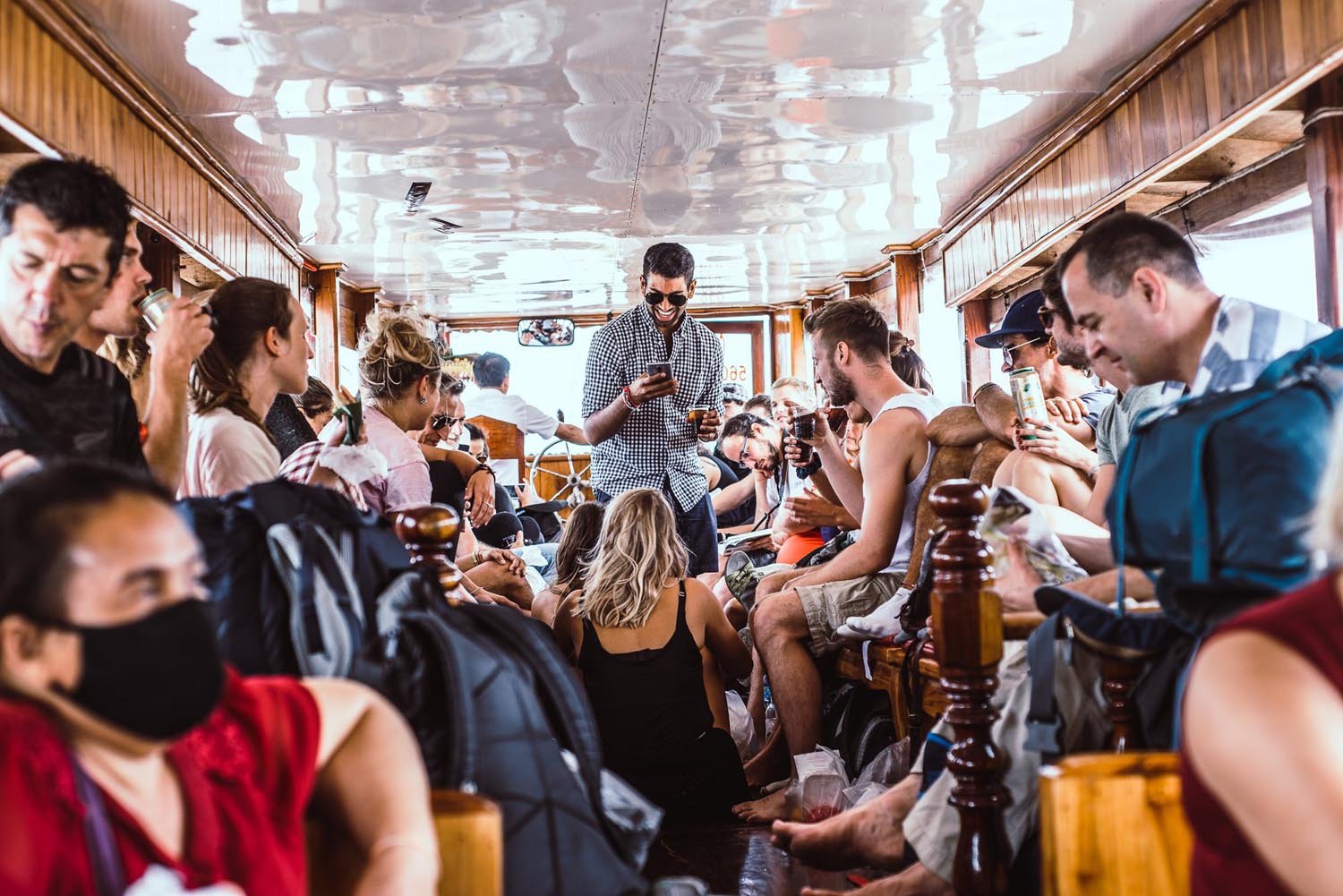 Group of people on a crowded boat interior, socializing and drinking.