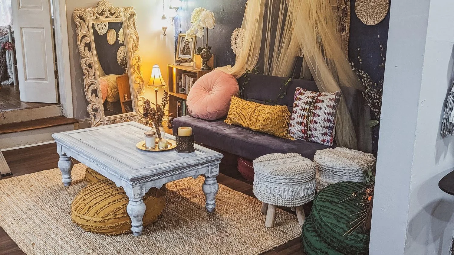 Cozy living room with a vintage mirror, stylish cushions on a navy sofa, rustic coffee table with candles, woven stools, and decorative elements.