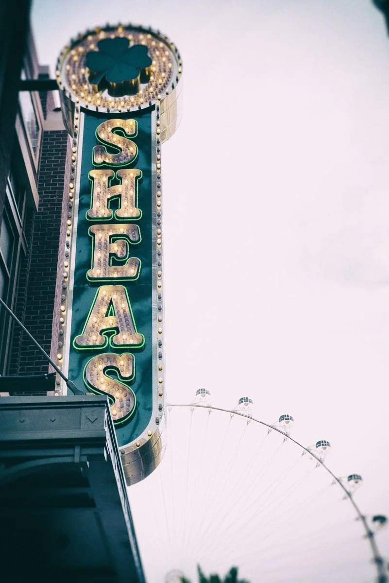 Vintage sign for Shea's with a clover design and lit-up letters, next to a Ferris wheel.