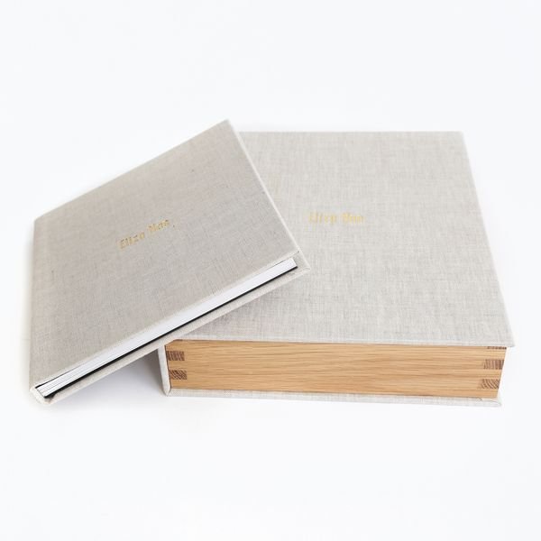 Two hardcover books with linen covers, one partially open, on a white background.