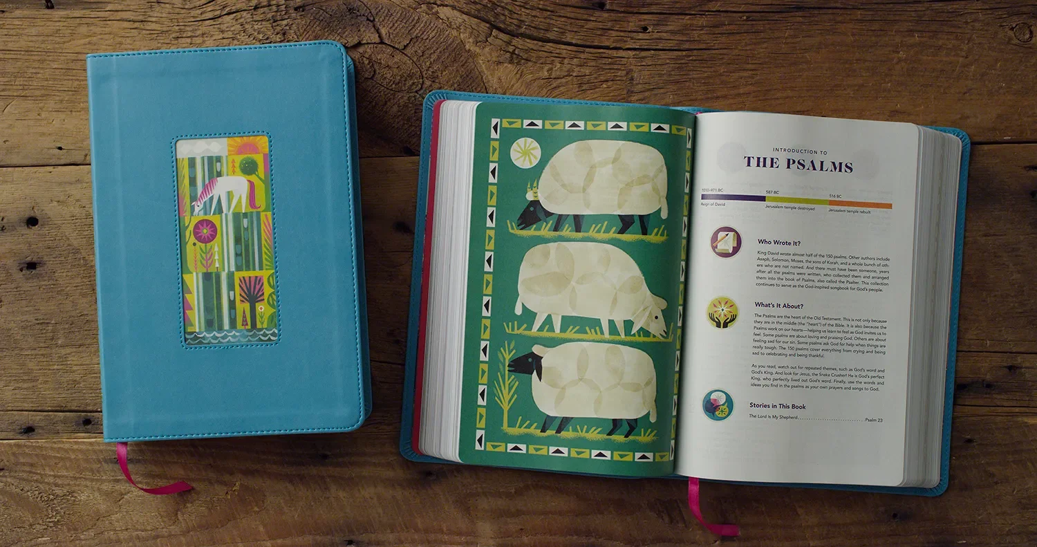 Open Bible with colorful illustrations and text about the Psalms, placed on a wooden table, with a closed blue cover Bible beside it.