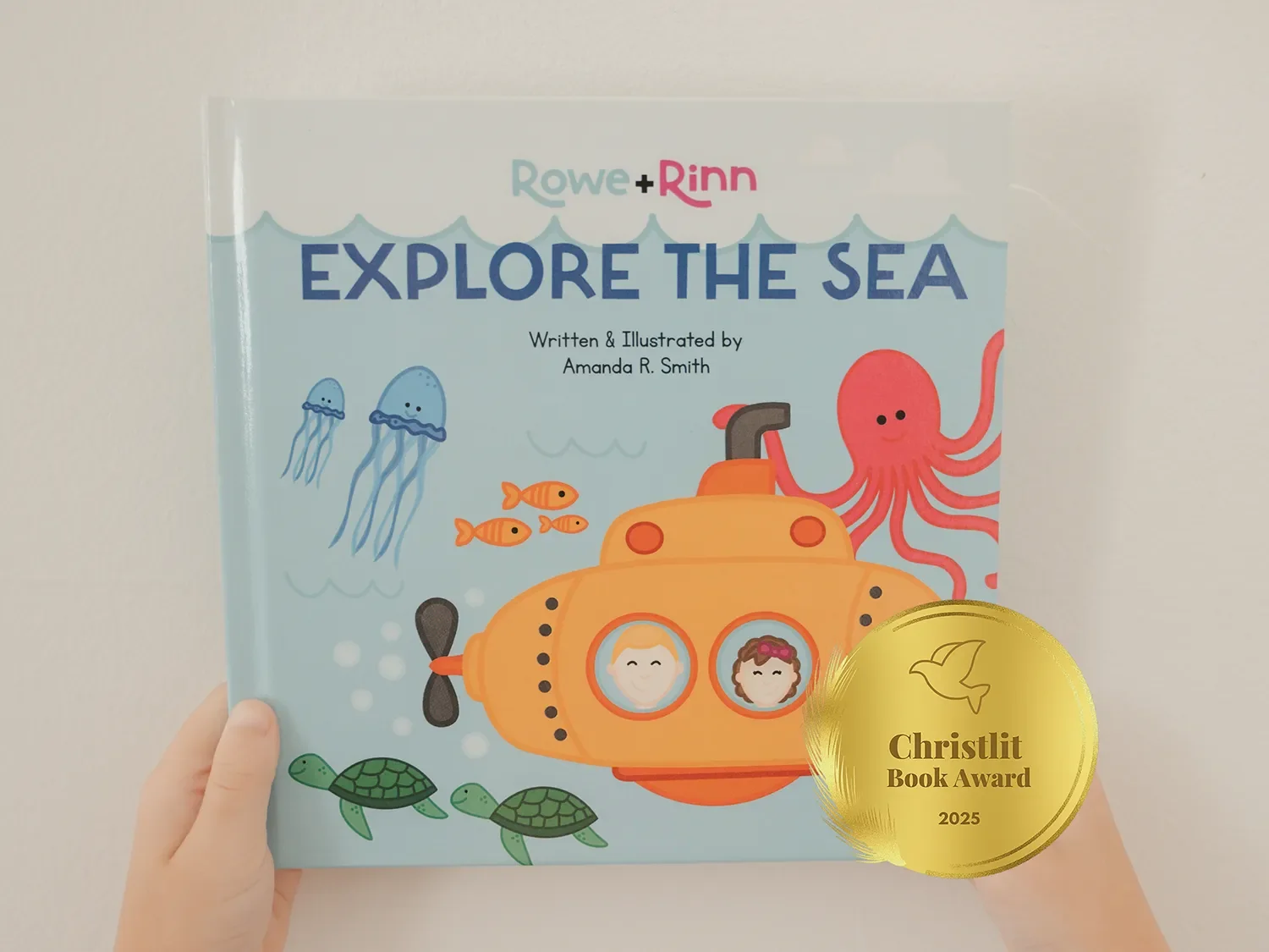 Children's book cover titled 'Explore the Sea' with illustrations of a yellow submarine, fish, turtles, jellyfish, and an octopus. Two children are visible in the submarine's windows. Hands are holding the book.