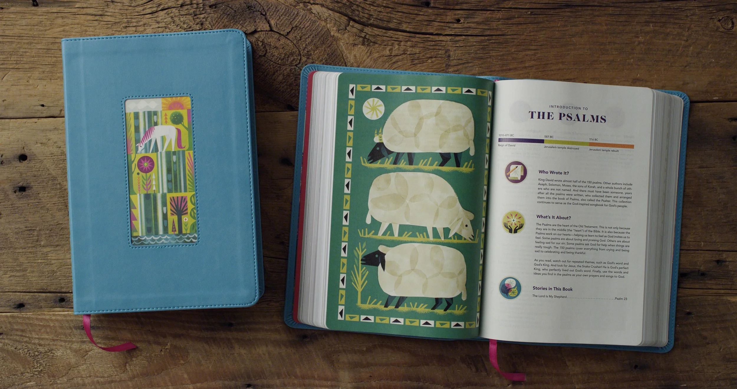 Open Bible with colorful illustrations and text about the Psalms, placed on a wooden table, with a closed blue cover Bible beside it.