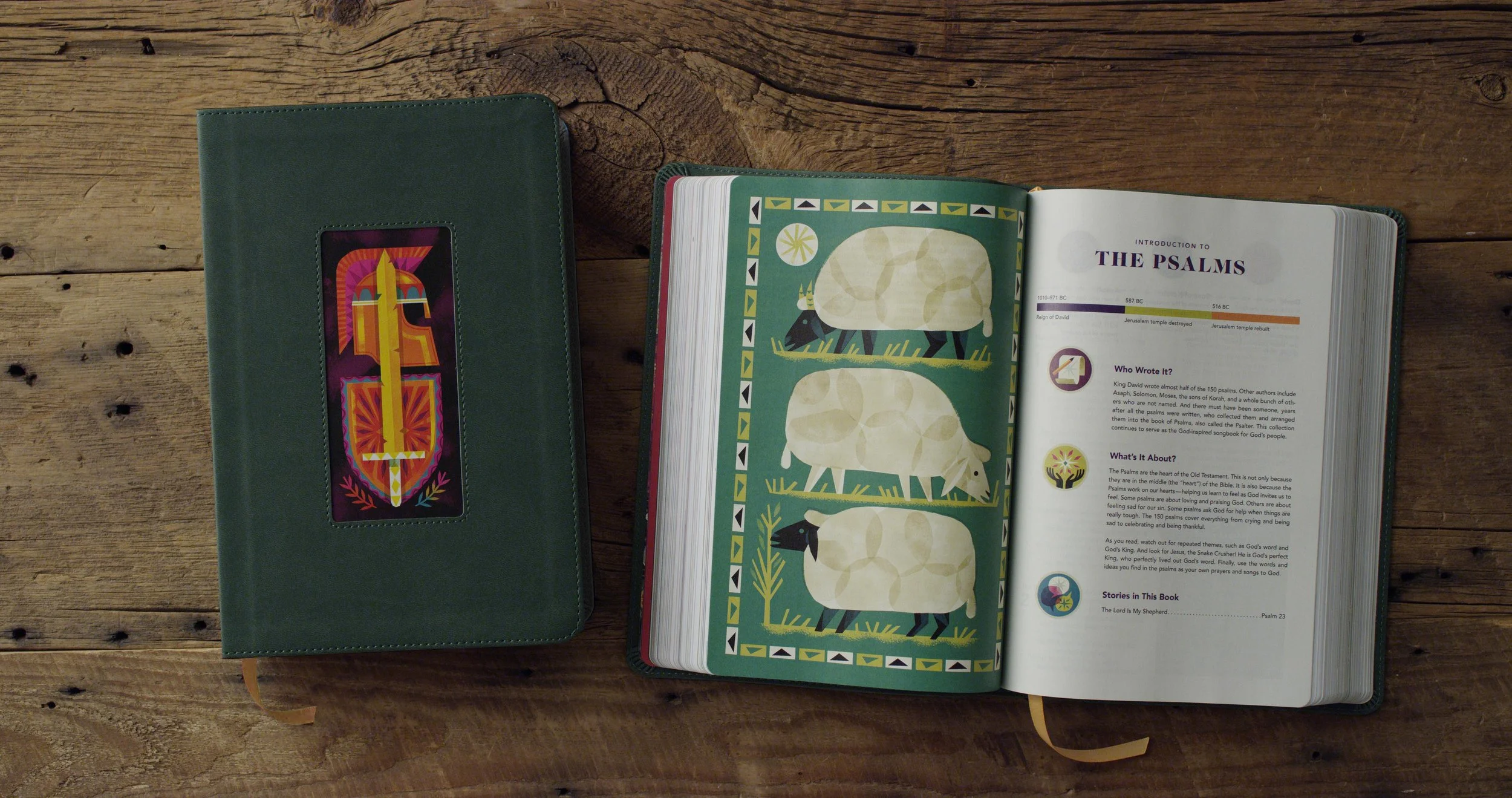 An open Bible displaying a colorful illustration of three sheep and a page about the Psalms, placed on a wooden surface next to a green journal with a decorative emblem on the cover.