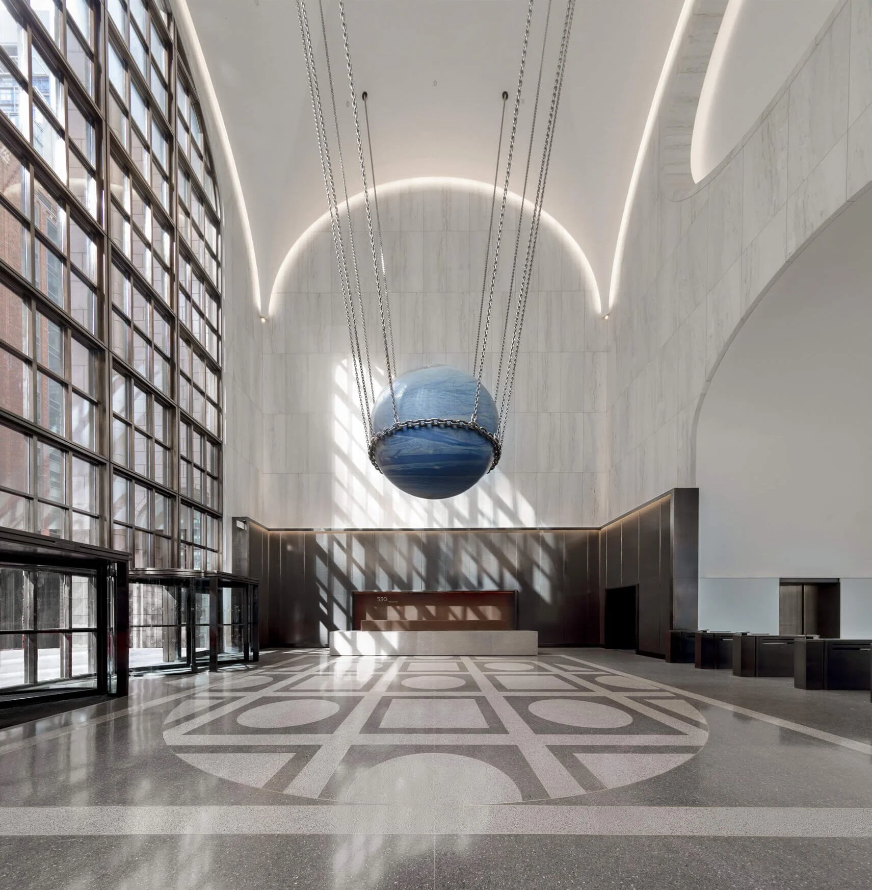 Alicja Kwade's Solid Sky hangs on chains in 550 Madison's marble lobby above a patterned terrazzo floor.