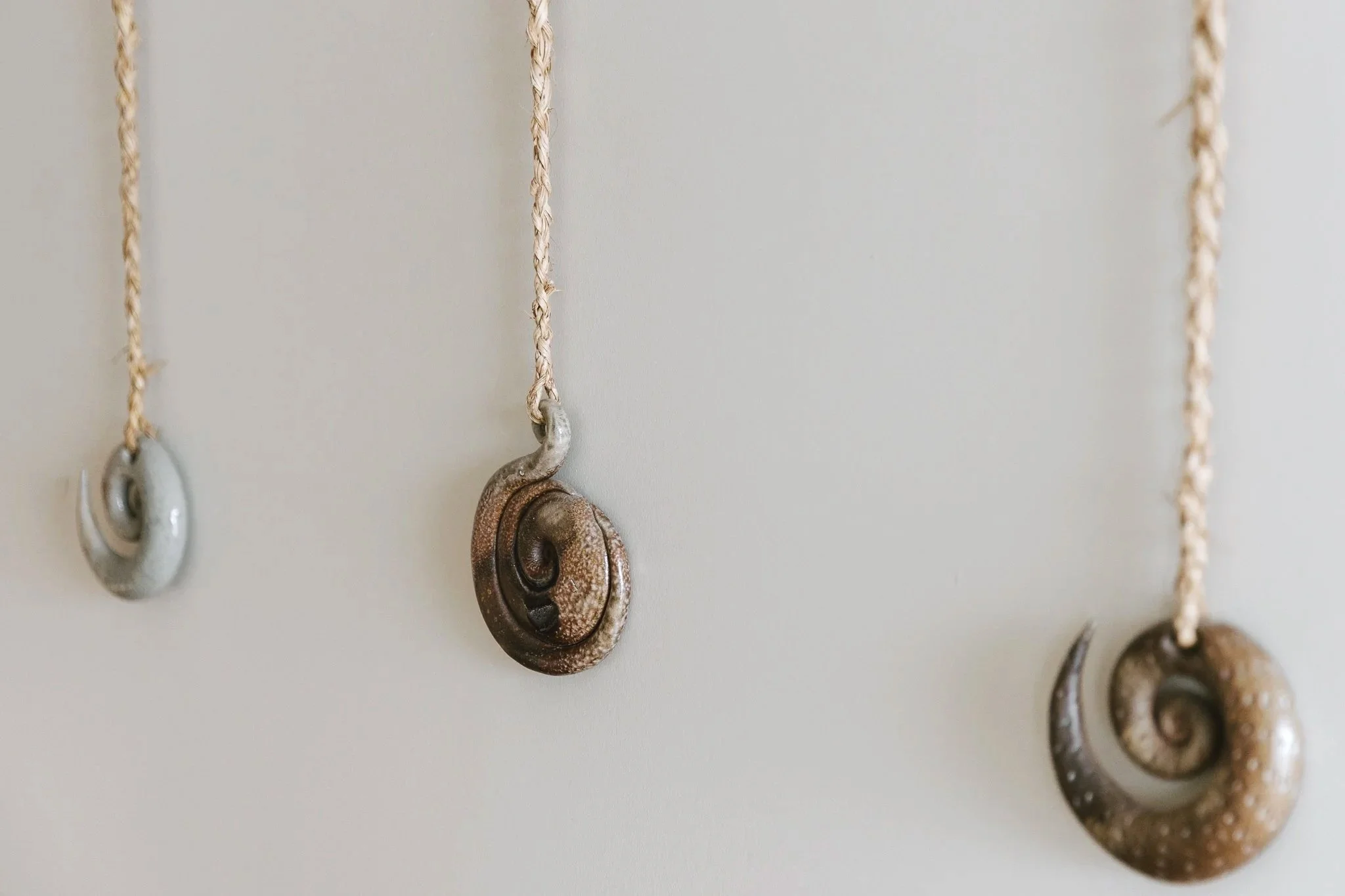 Close-up of several spiral-shaped shell necklaces hanging on a wall, with the shells varying in size and color.