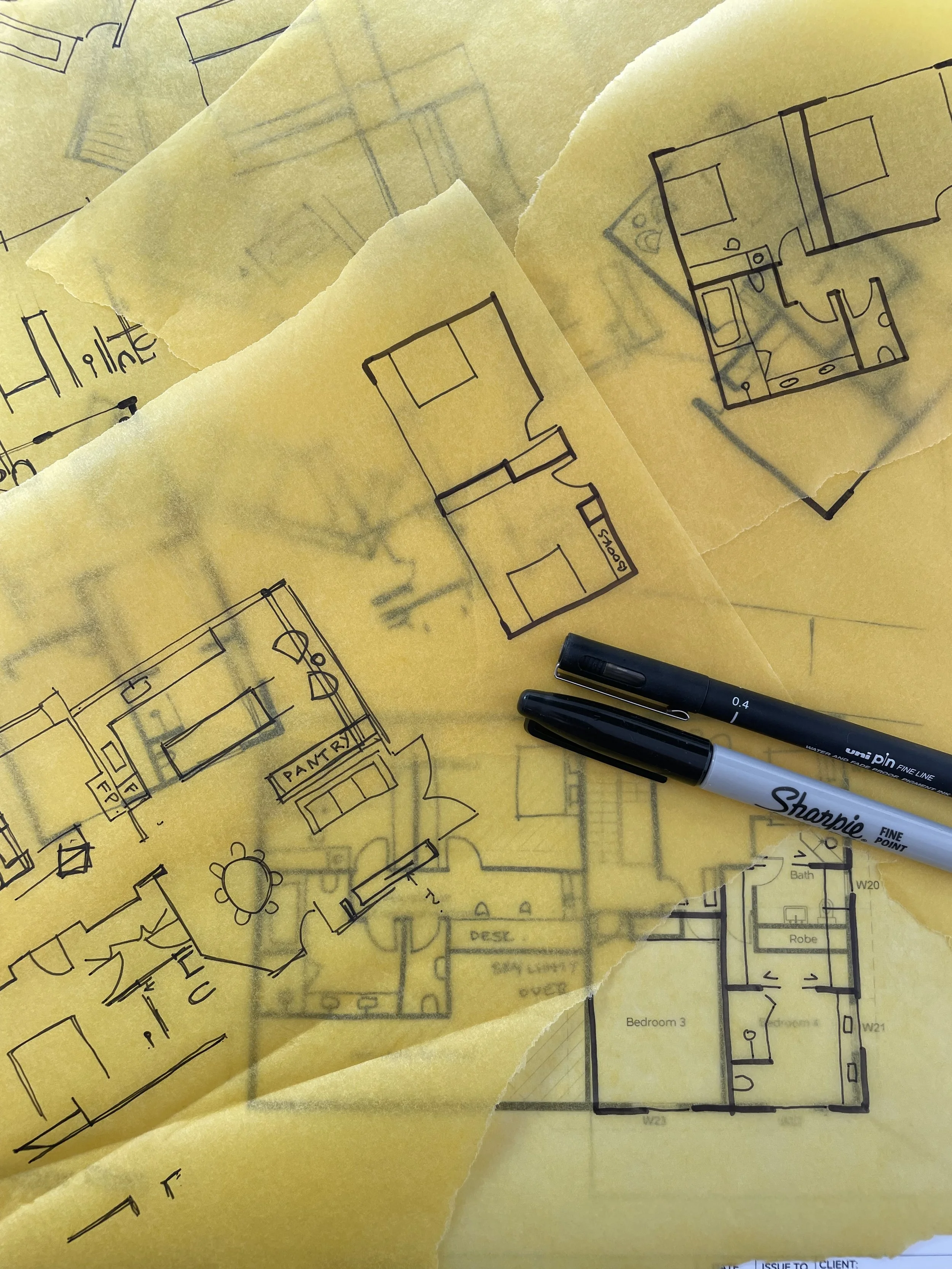 Blueprints of house floor plans on yellow translucent paper with pens.