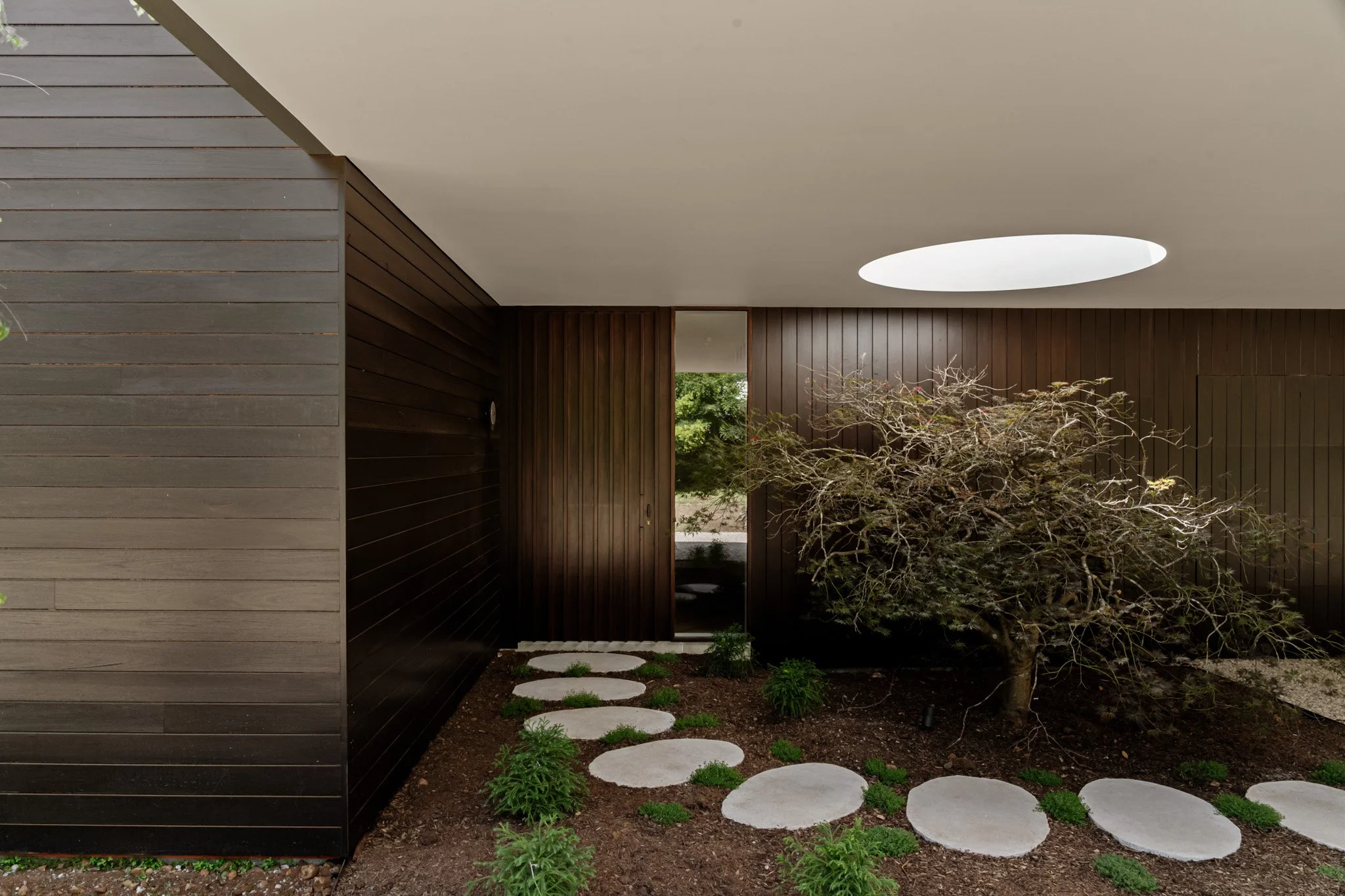 Entry courtyard with circular skylight, dark timber cladding and landscaped garden in a Southern Highlands home