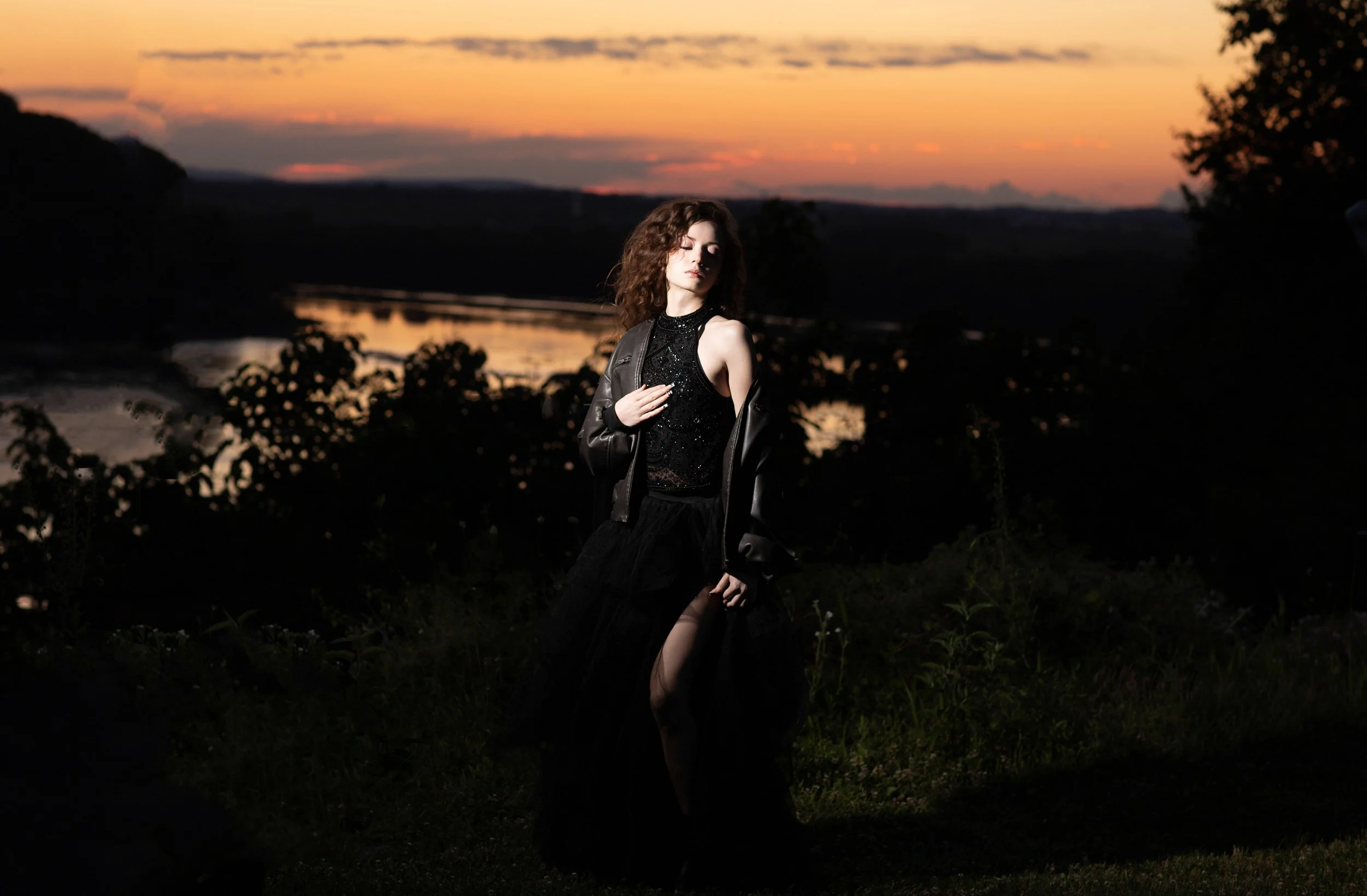 High school senior in a flowing black gown posing at sunset overlooking the Susquehanna River in Lancaster, Pennsylvania, creating a dramatic outdoor senior portrait with golden skies and scenic river views.