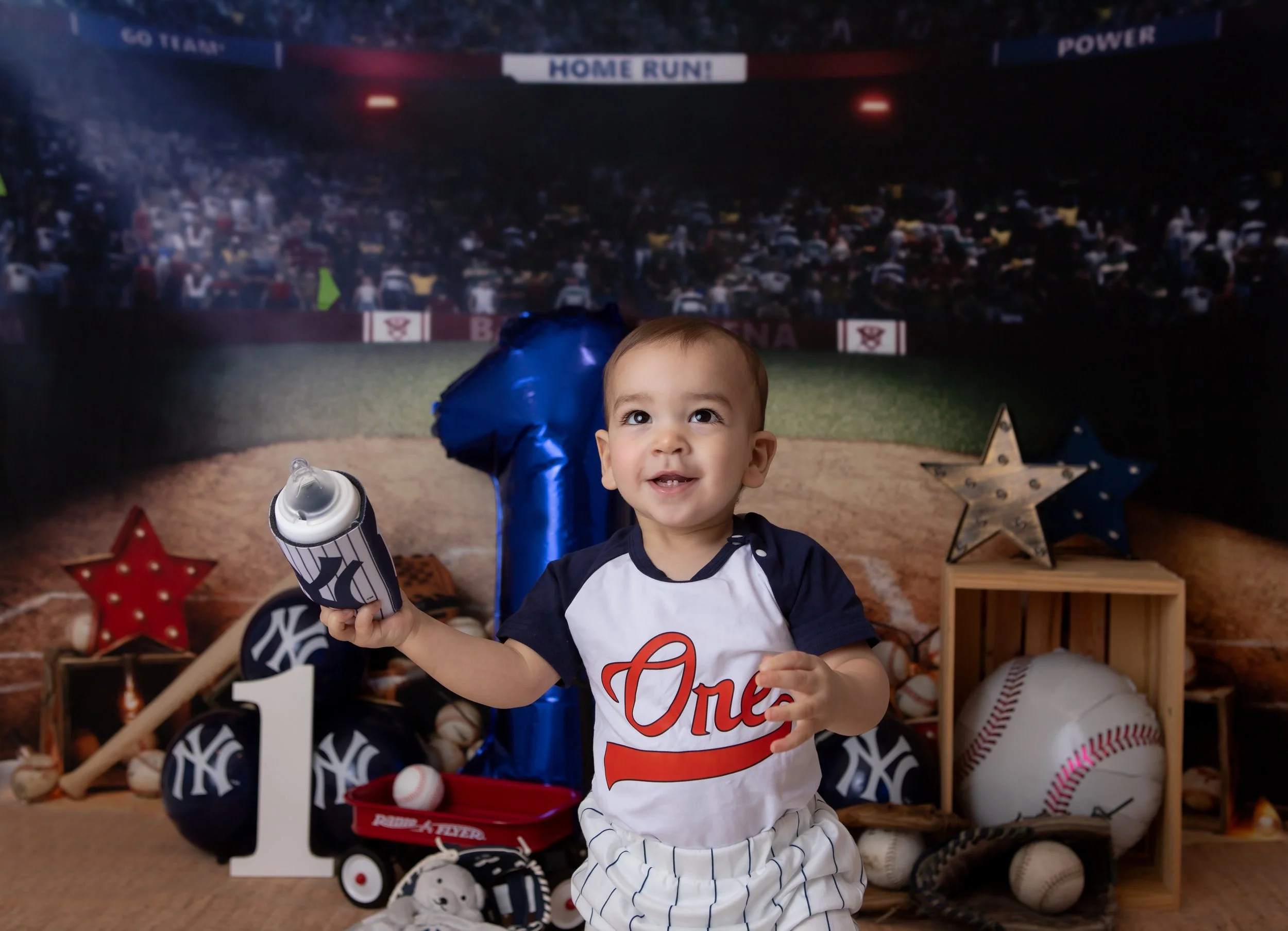 a smiling one year old boy looking up and holding a new york yankees team cup