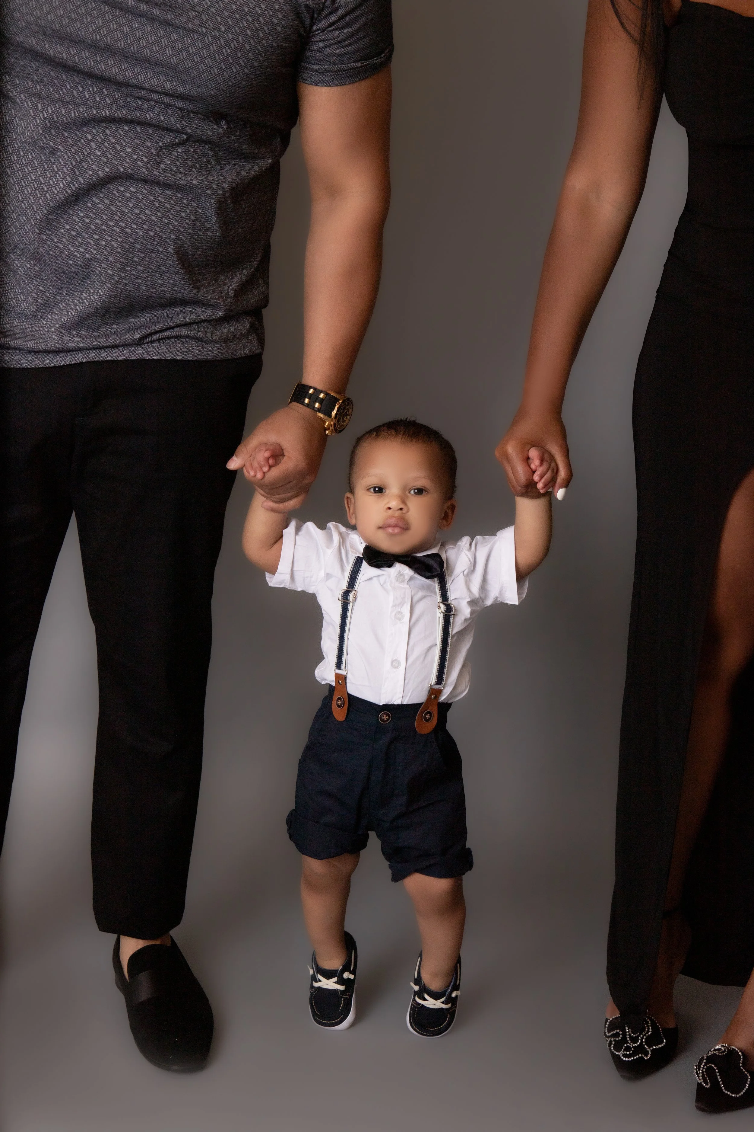 little boy wearing bow tie and suspenders holding hands with his parents