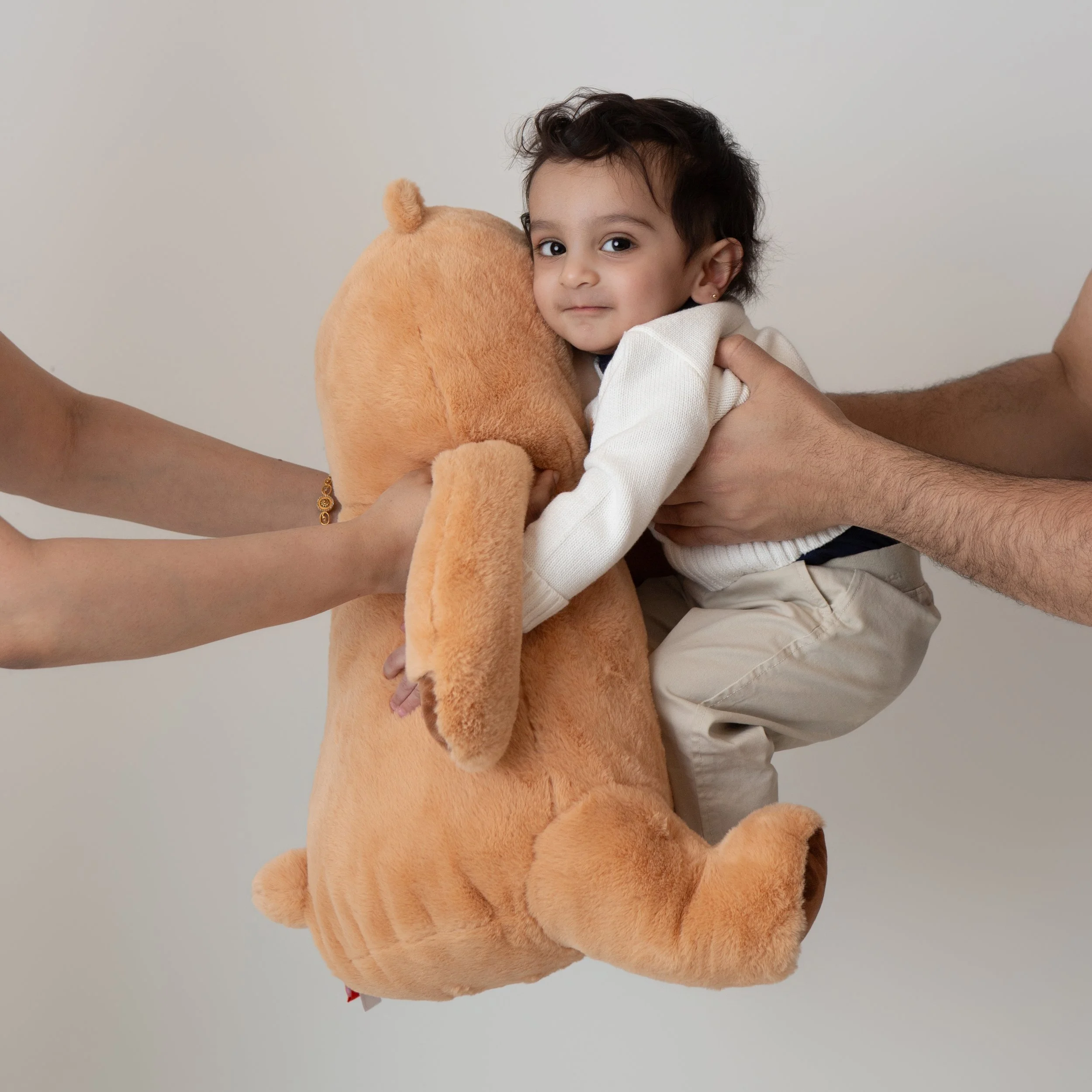 parents holding a smiling one year old boy hugging a large stuffed bear 