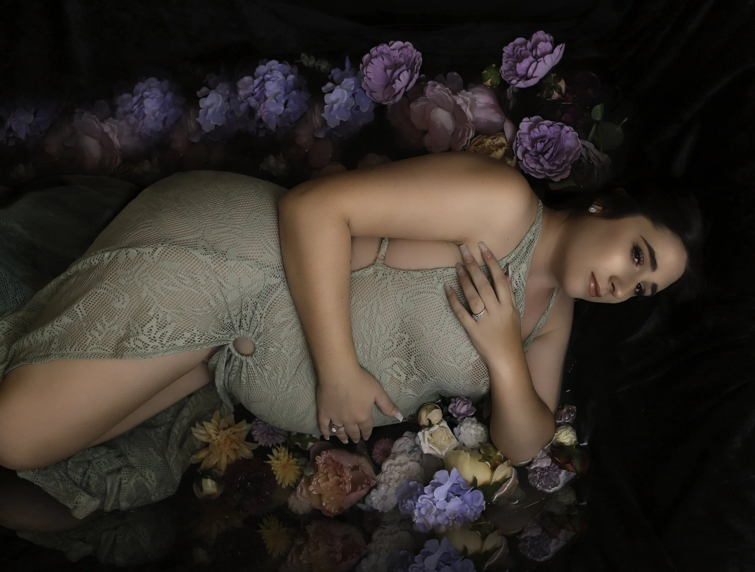 pregnant women in water wearing a green lace dress surrounded by flowerw