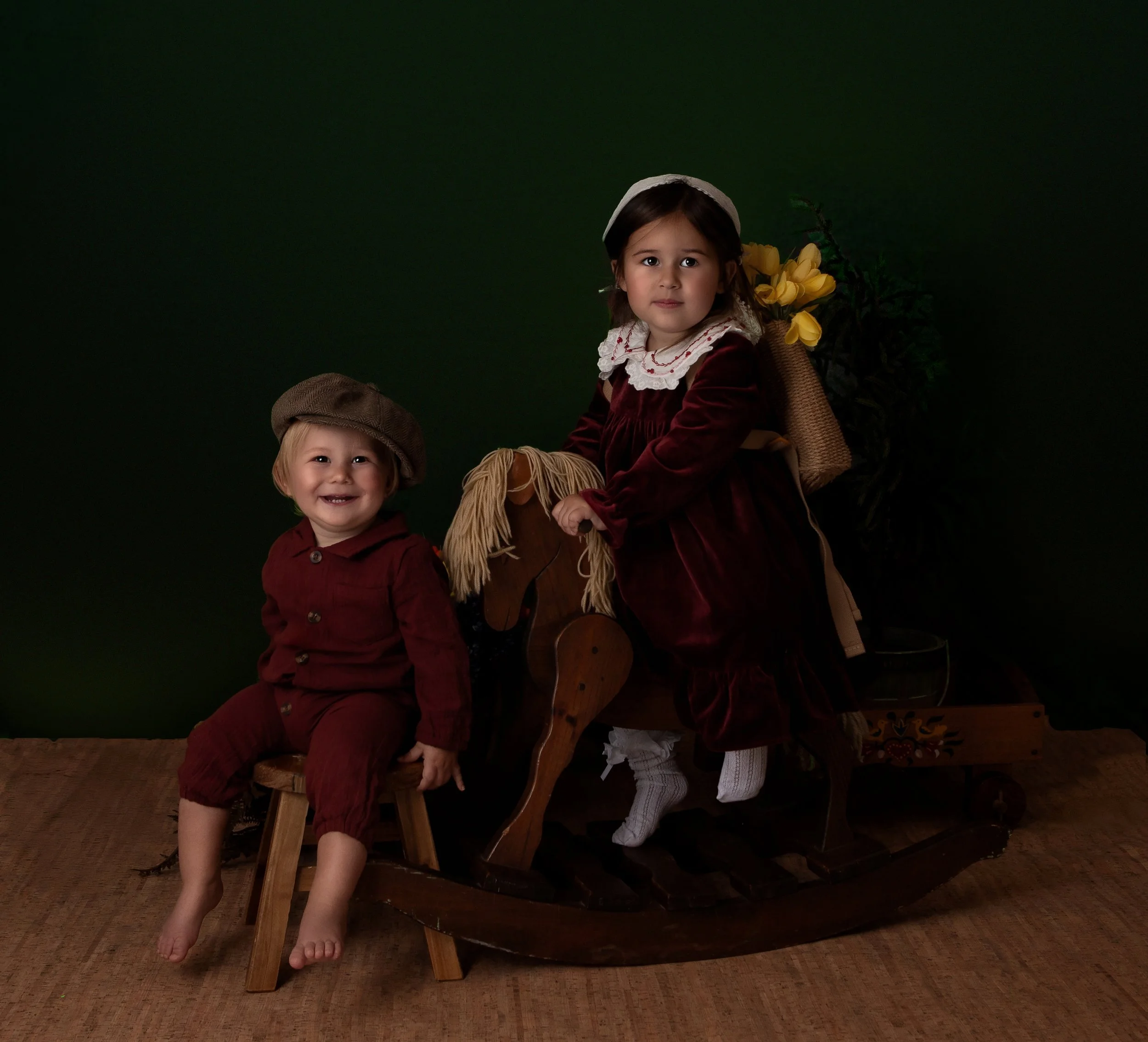 a little boy and girl smiling wearing red outfits with little girl sitting on a wooden rockng horse