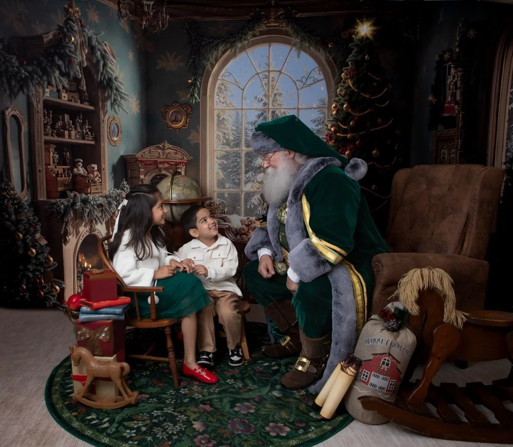a little boy ande girl sitting and smiling with Santa talking to them 