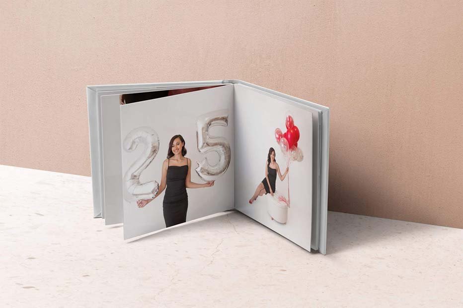 Open photo album featuring a young woman celebrating her 25th birthday with silver number balloons and red balloons in a minimalist studio setting. Custom heirloom photo book in Lancaster, PA.