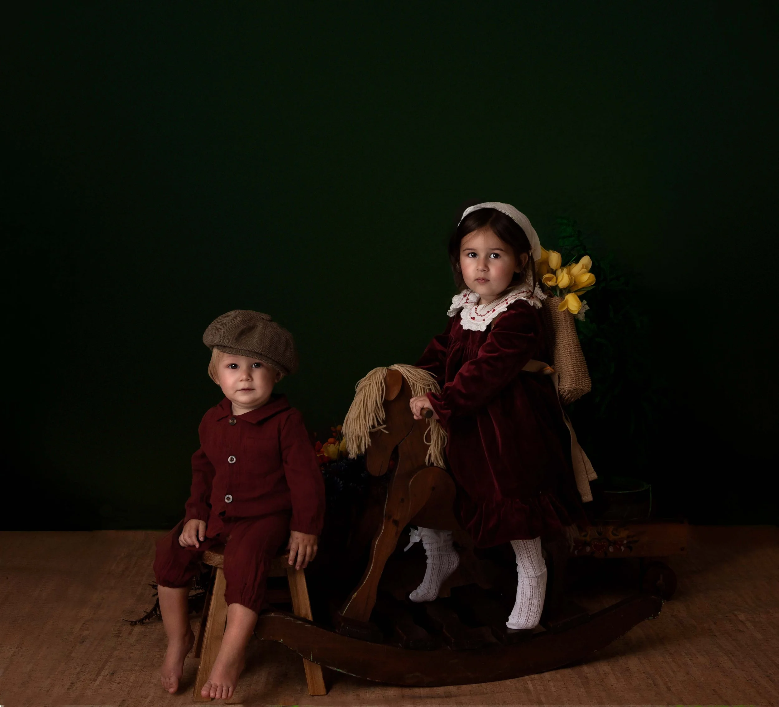 a little girl and little boy with solenm faces both wearing red outifts with caps on their head