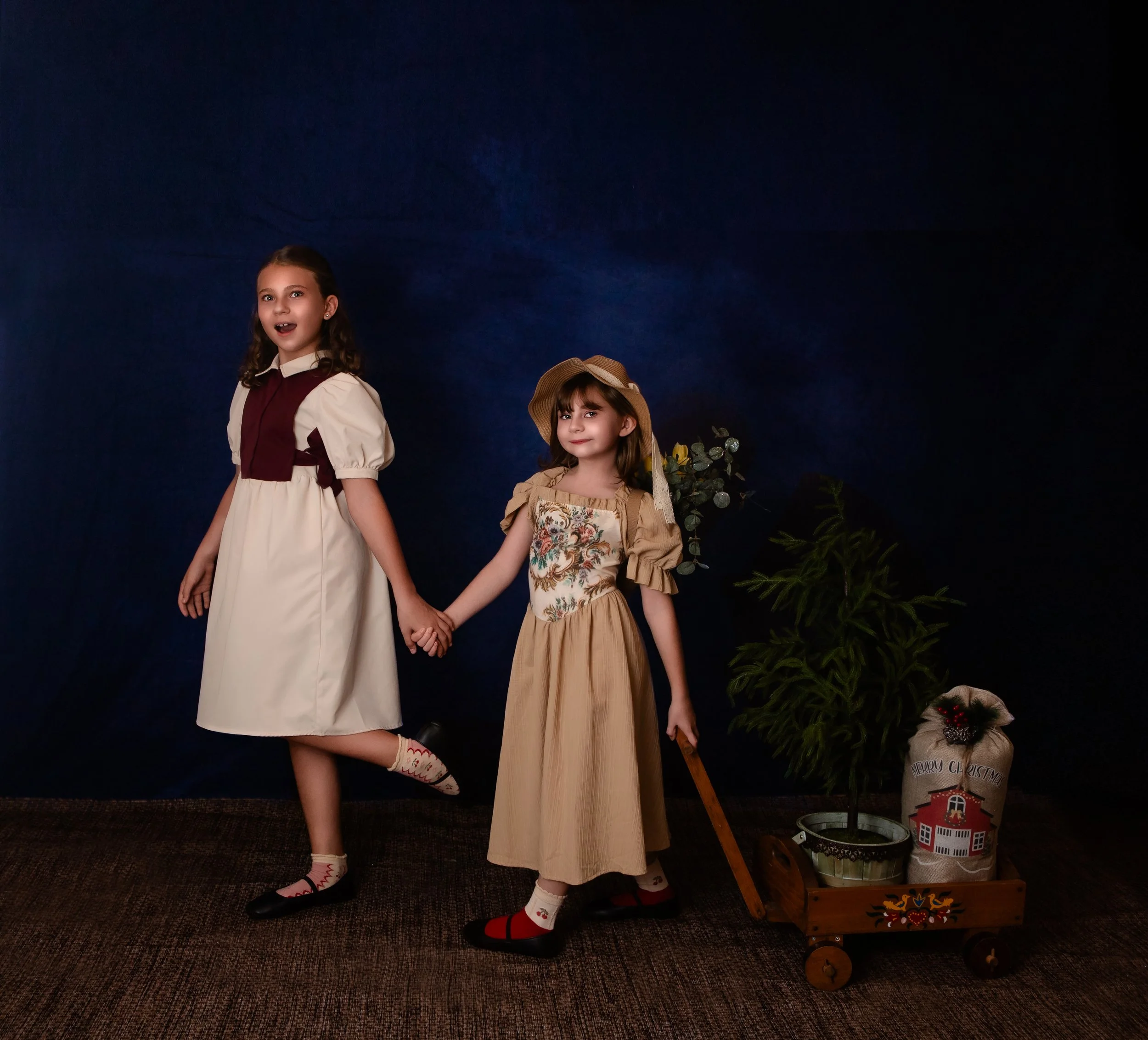 two girls holding hands smiling and one girl pulling a wagon