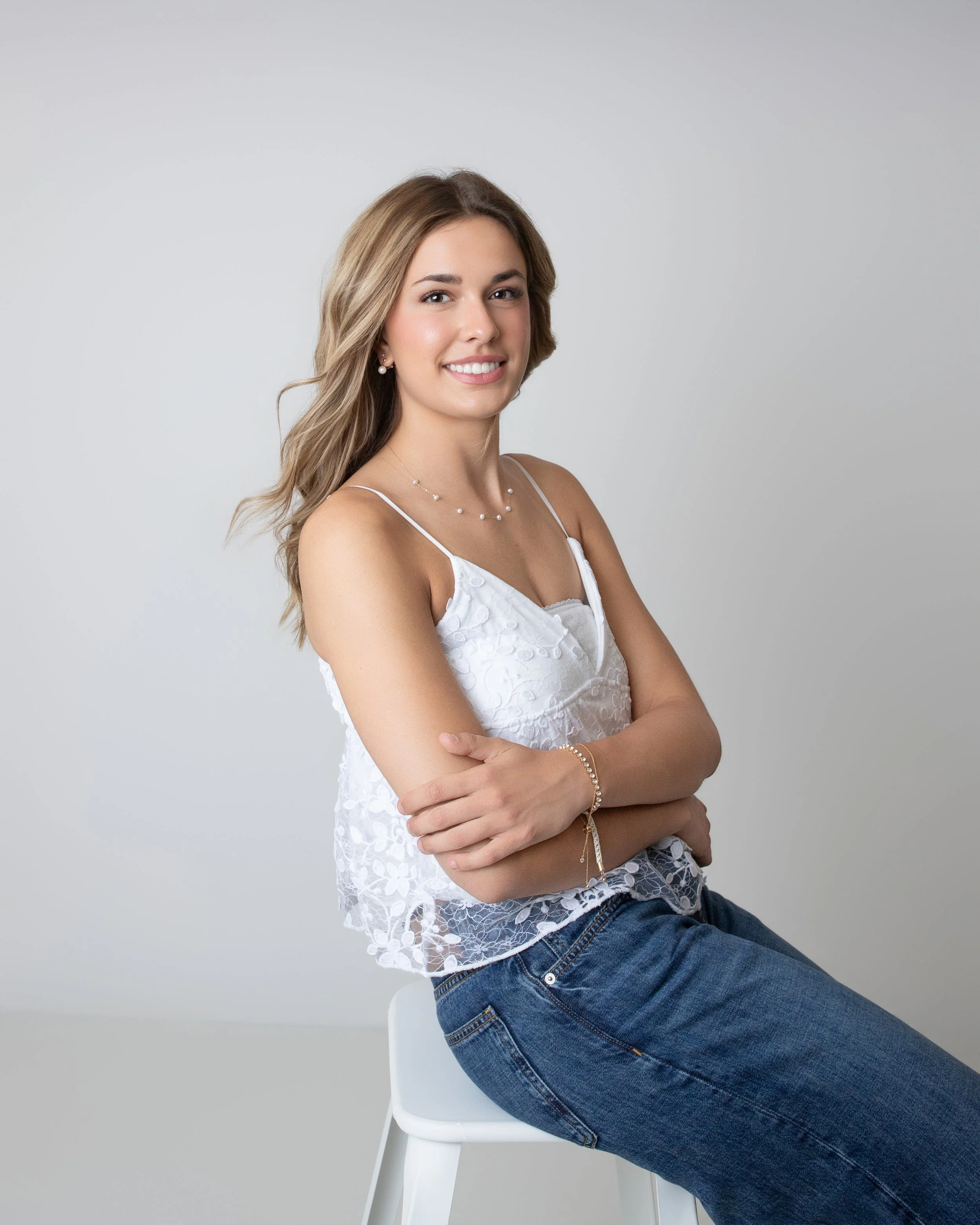 High school senior portrait of a smiling teenage girl in casual jeans and a white top hair blowing photographed in a professional studio by Lancaster PA senior photographer Kat DiComo Photography.