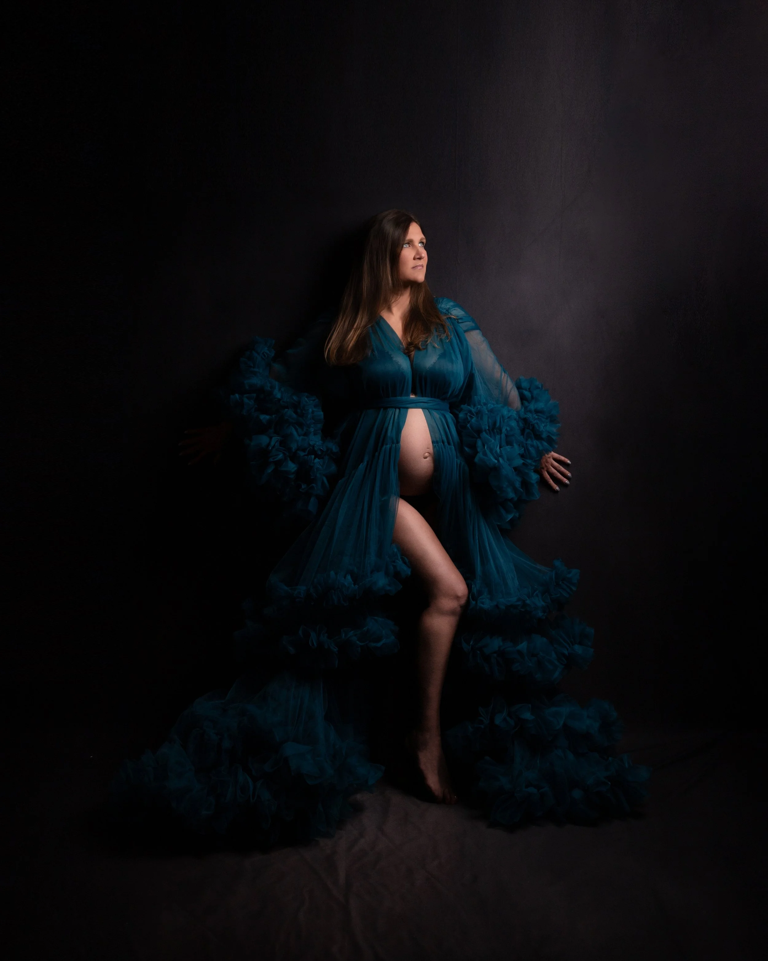 a pregnant woman wearing a blue ruffled robe with her tummy showing 
